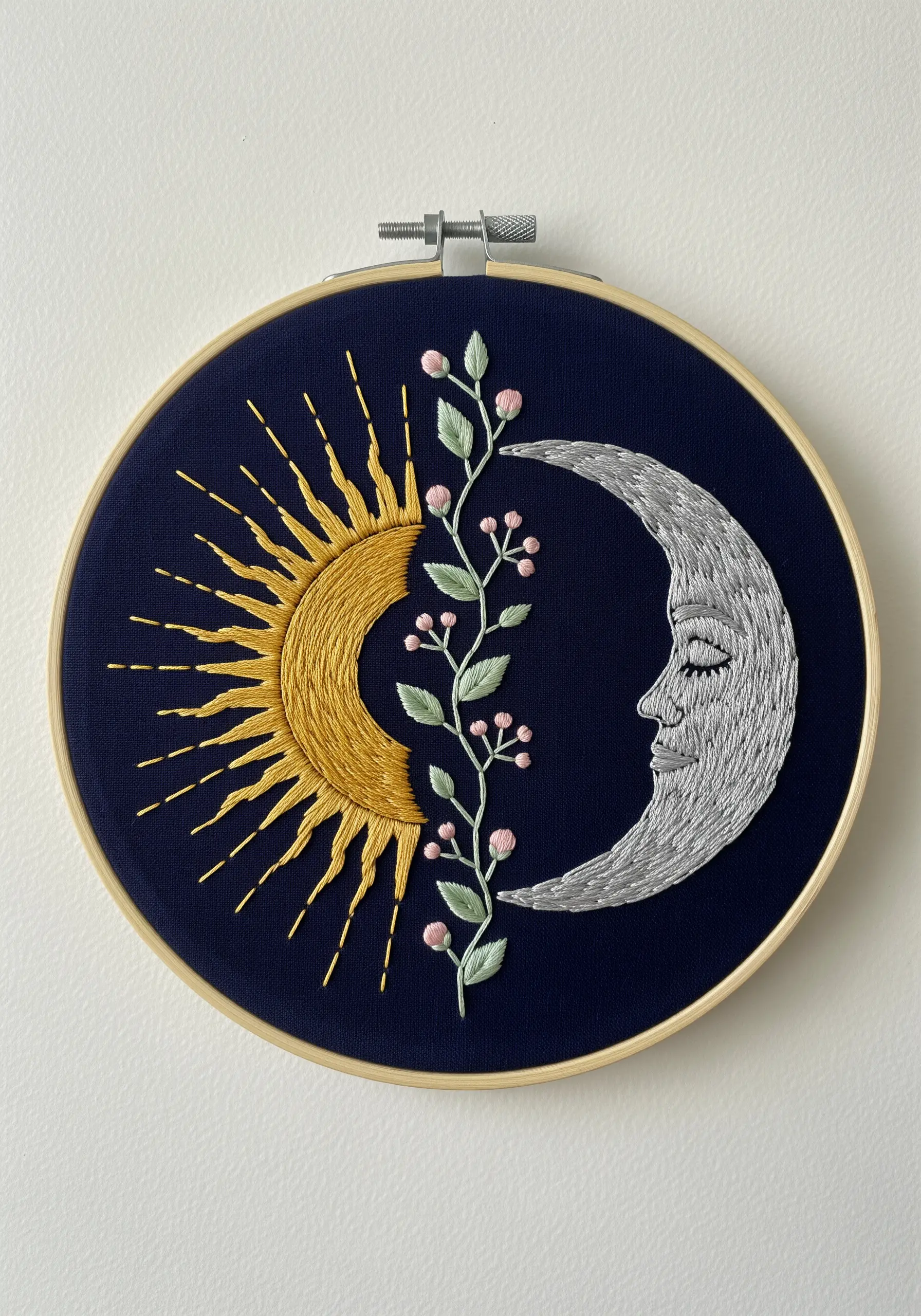 Embroidered sun and moon separated by a floral vine on dark blue fabric.
