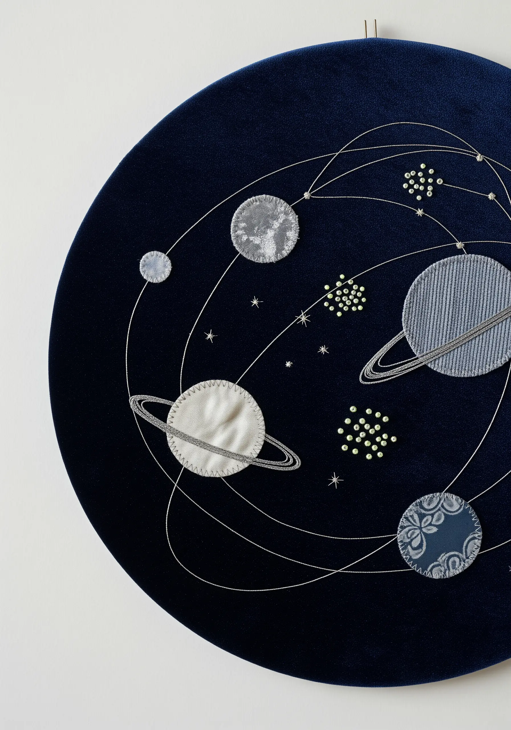 A cosmic scene on dark velvet with planets made from textured fabric scraps and beaded stars.