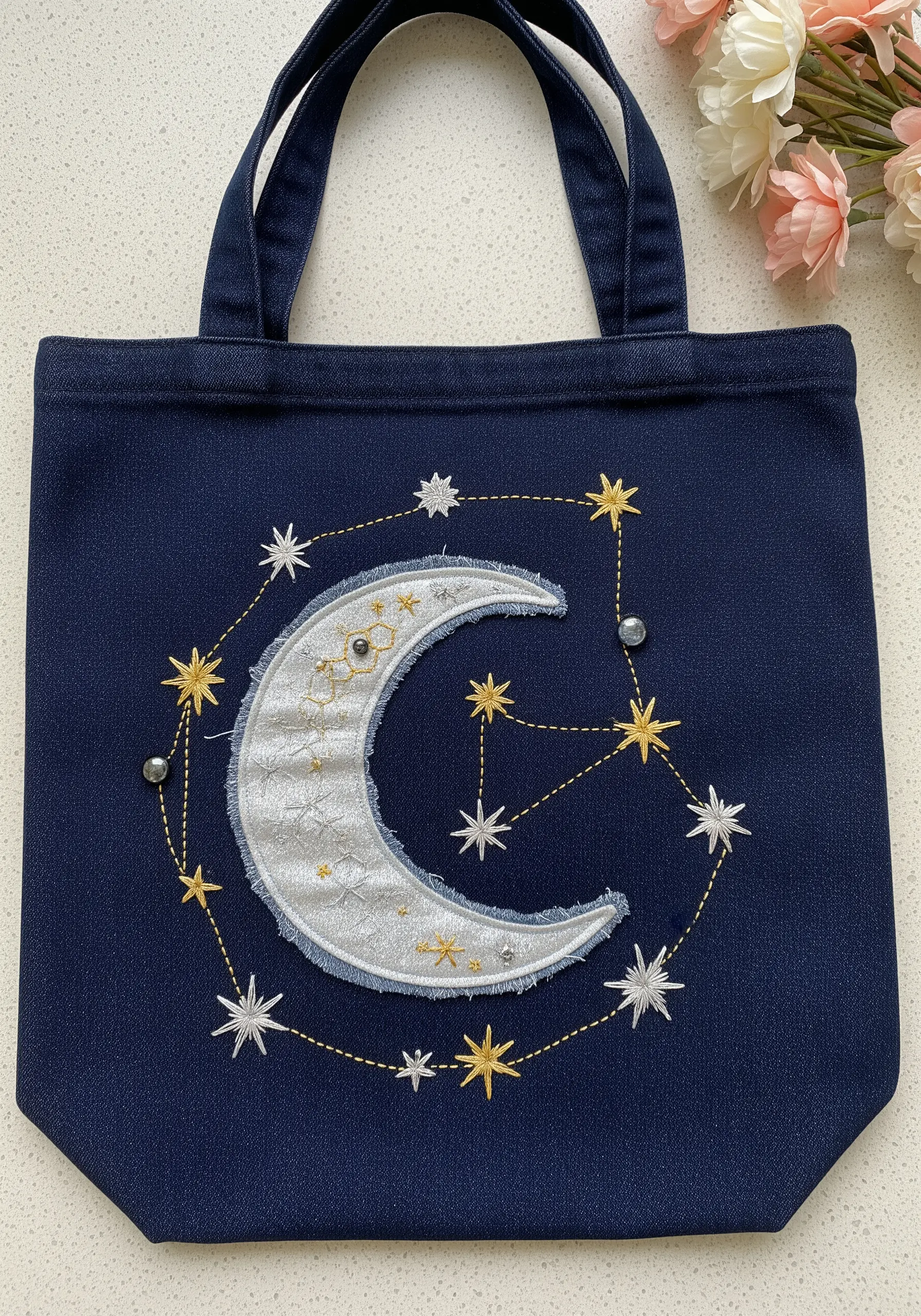 Crescent moon appliqué with metallic thread stars embroidered on a dark denim tote bag.