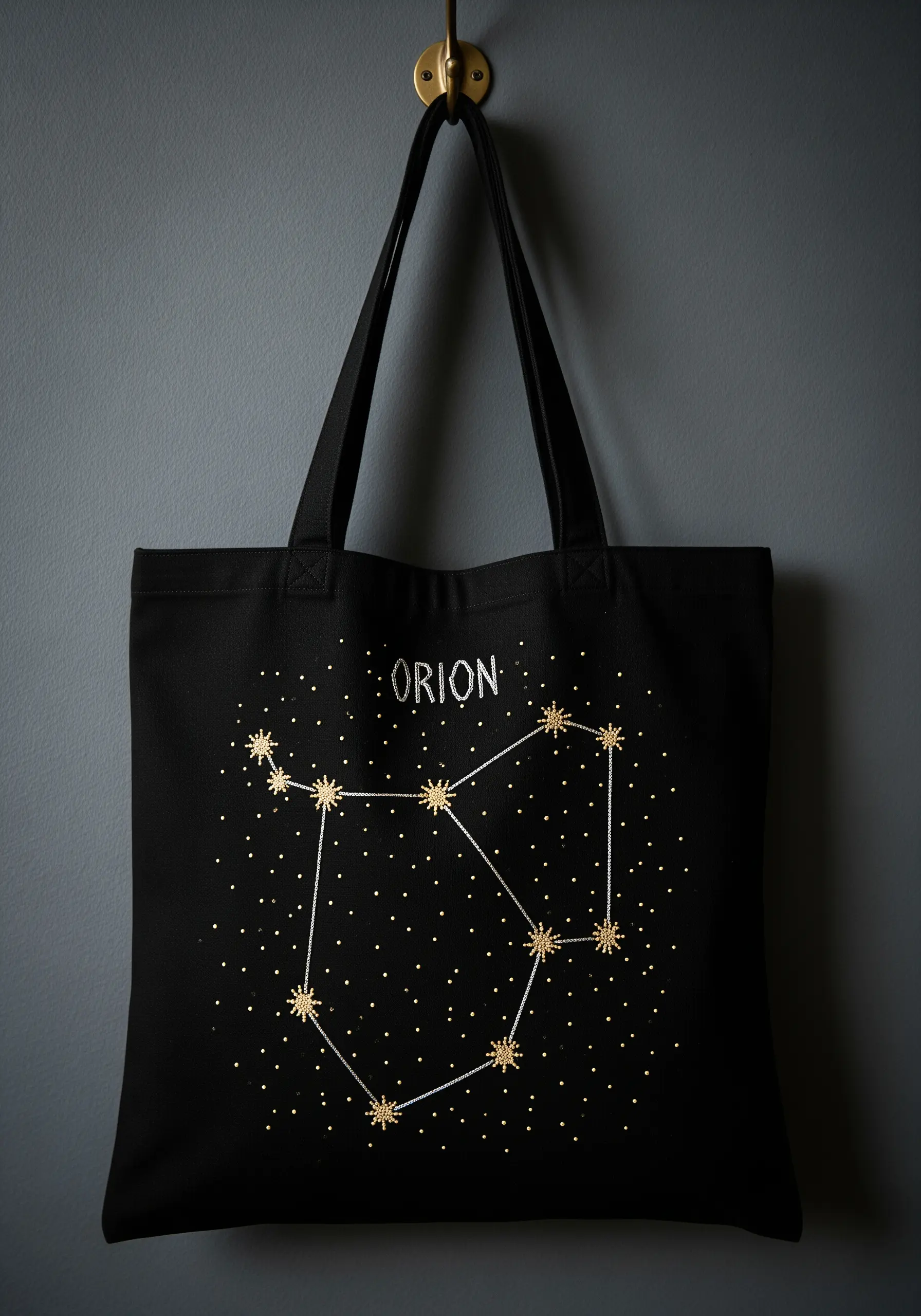 Embroidered Orion constellation with gold metallic thread stars on a black tote bag.