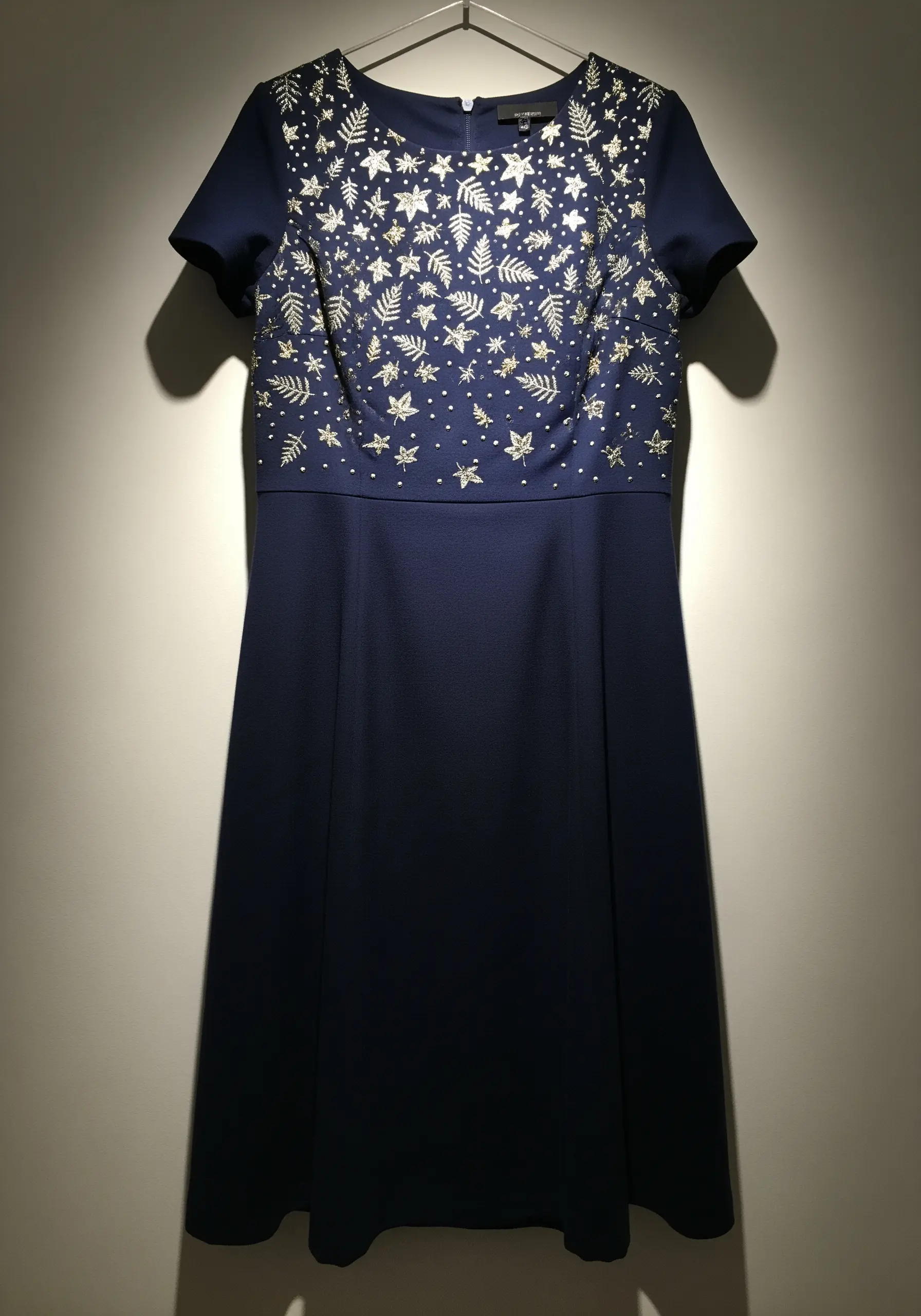 The bodice of a navy dress embroidered with a mix of silver leaves, stars, and dots.