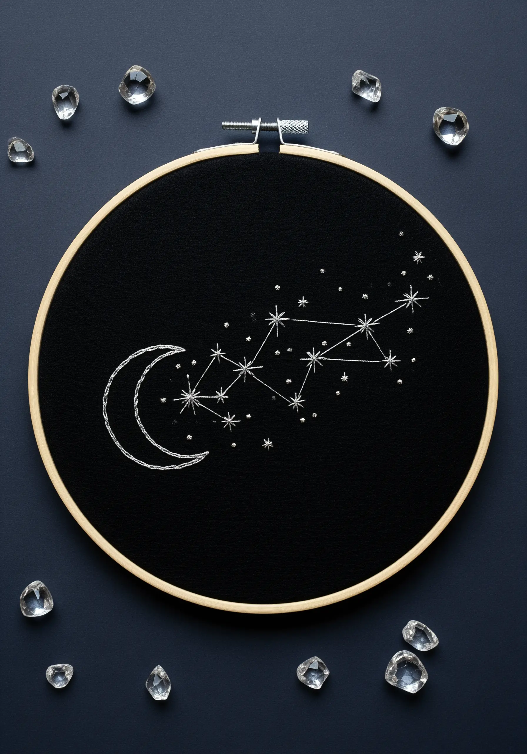 A crescent moon and star constellation embroidered in silver thread on black fabric.