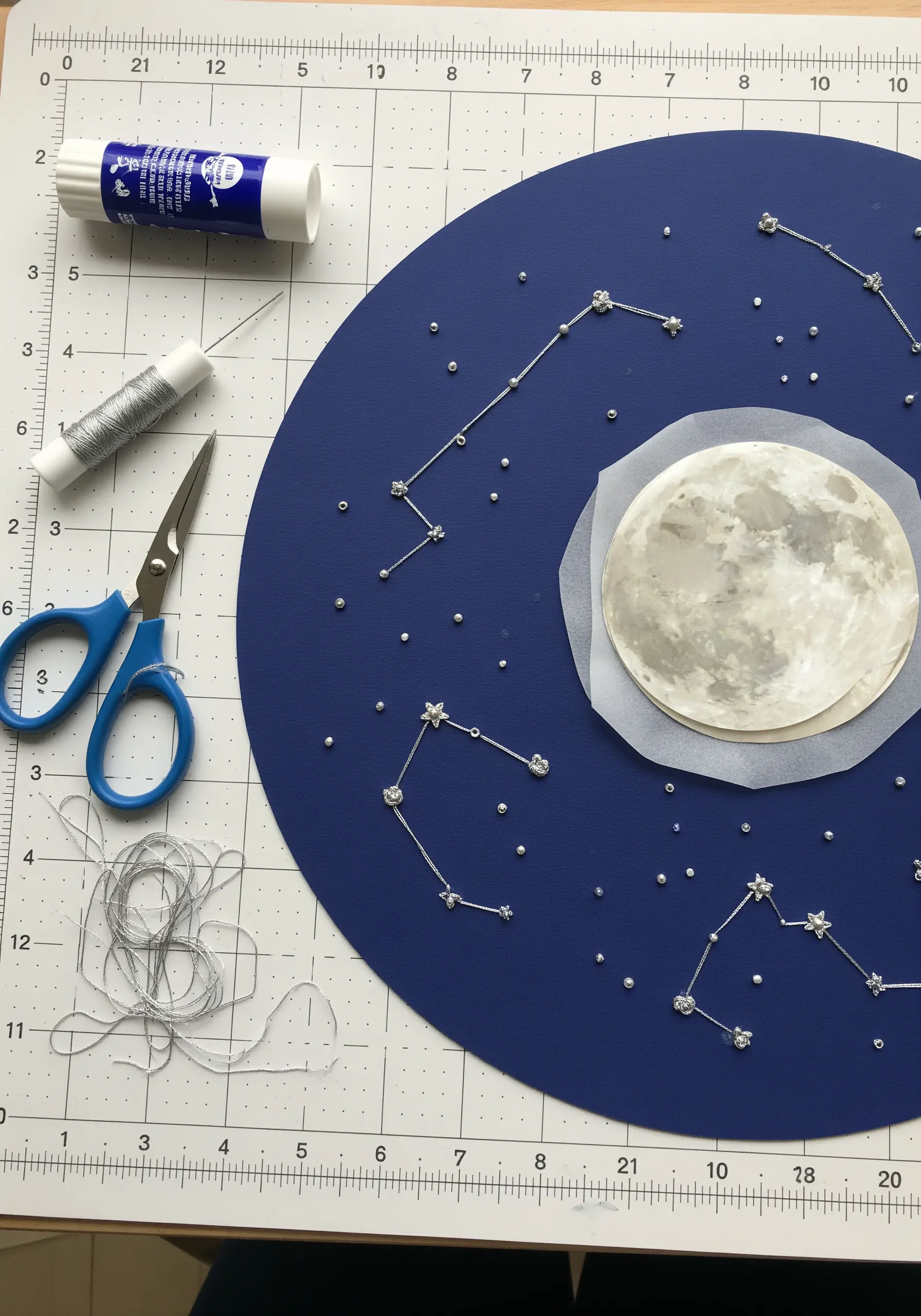 Stitched constellations using silver metallic thread and beads on dark blue paper.