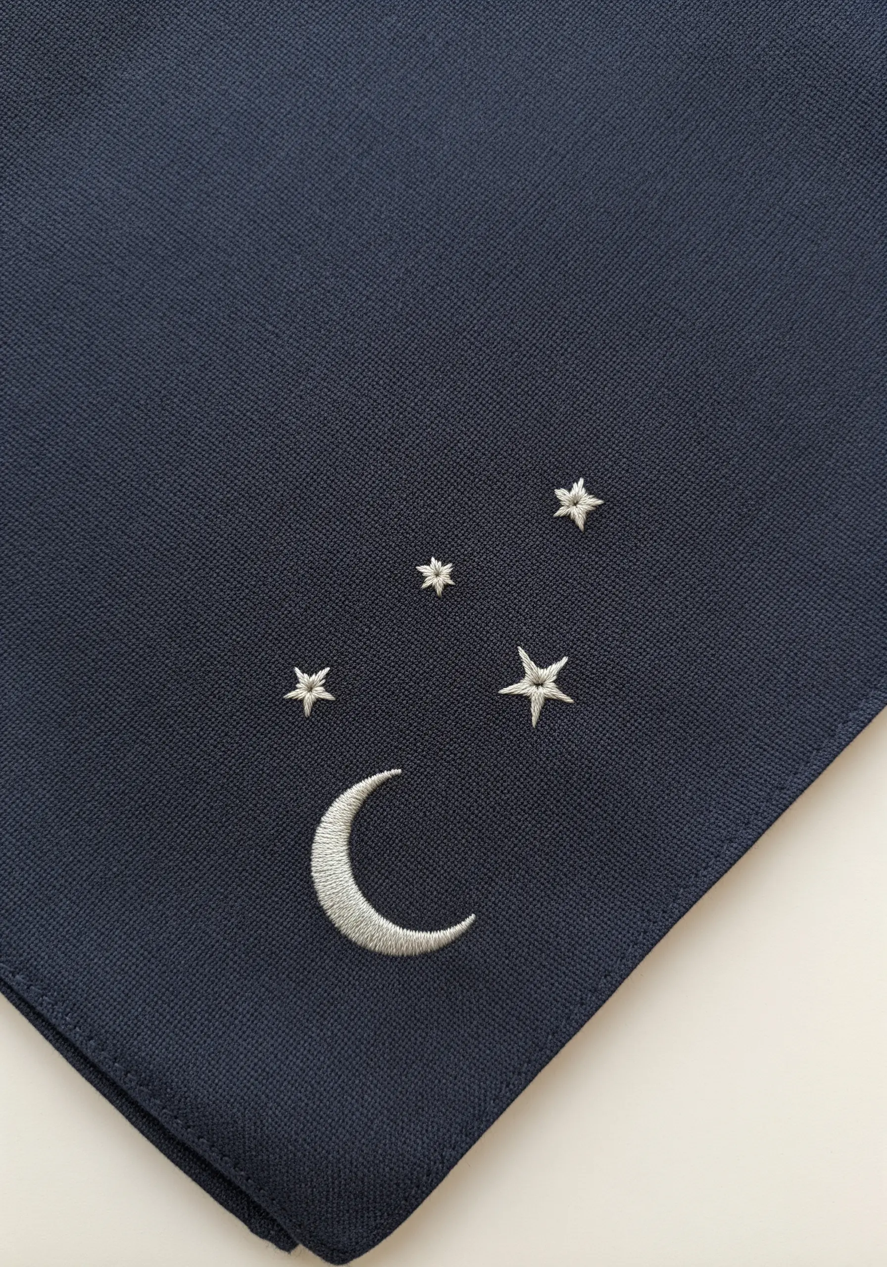 A silver crescent moon and stars embroidered on a dark blue handkerchief.