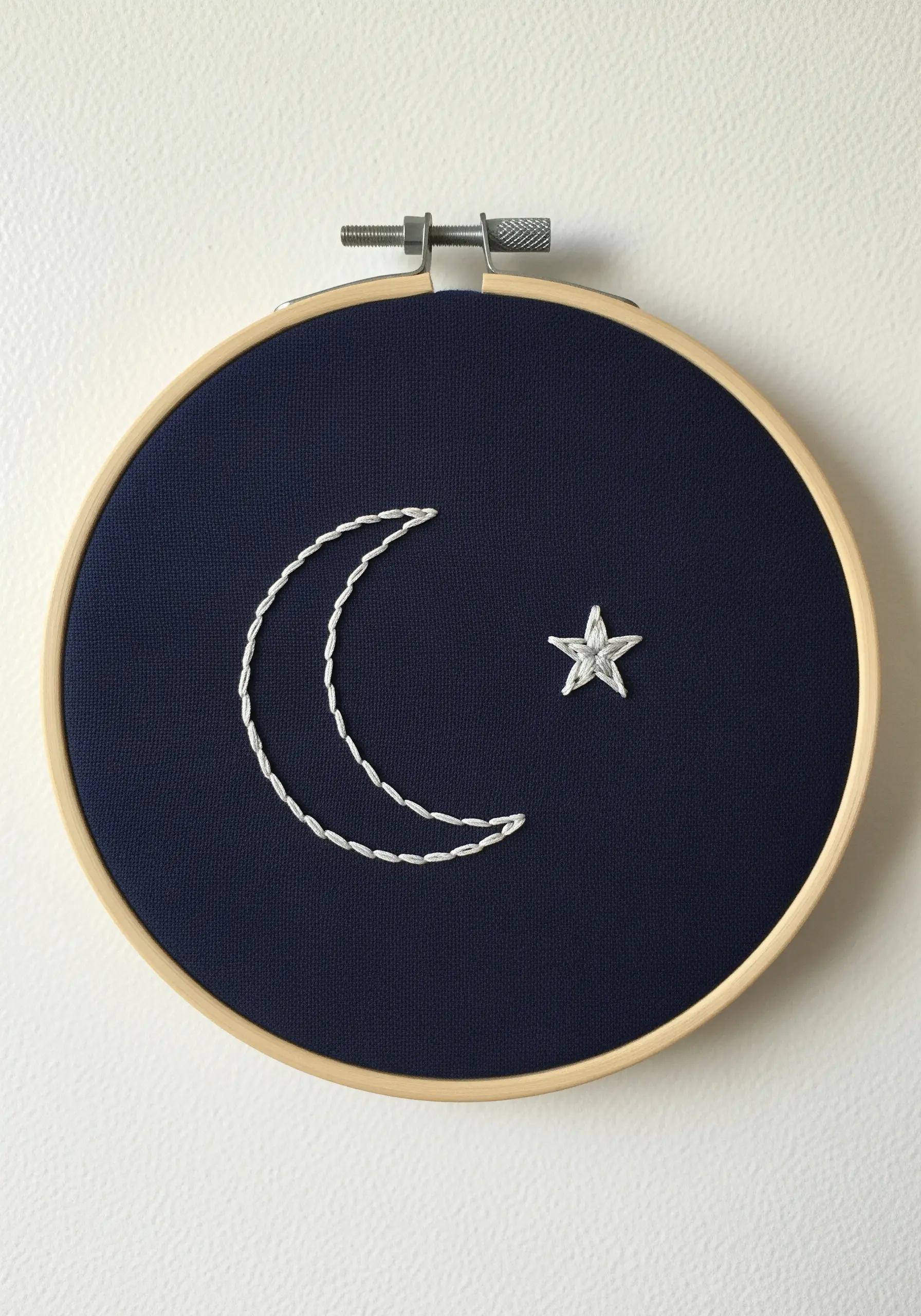 A simple crescent moon and star embroidered in white on dark blue fabric.