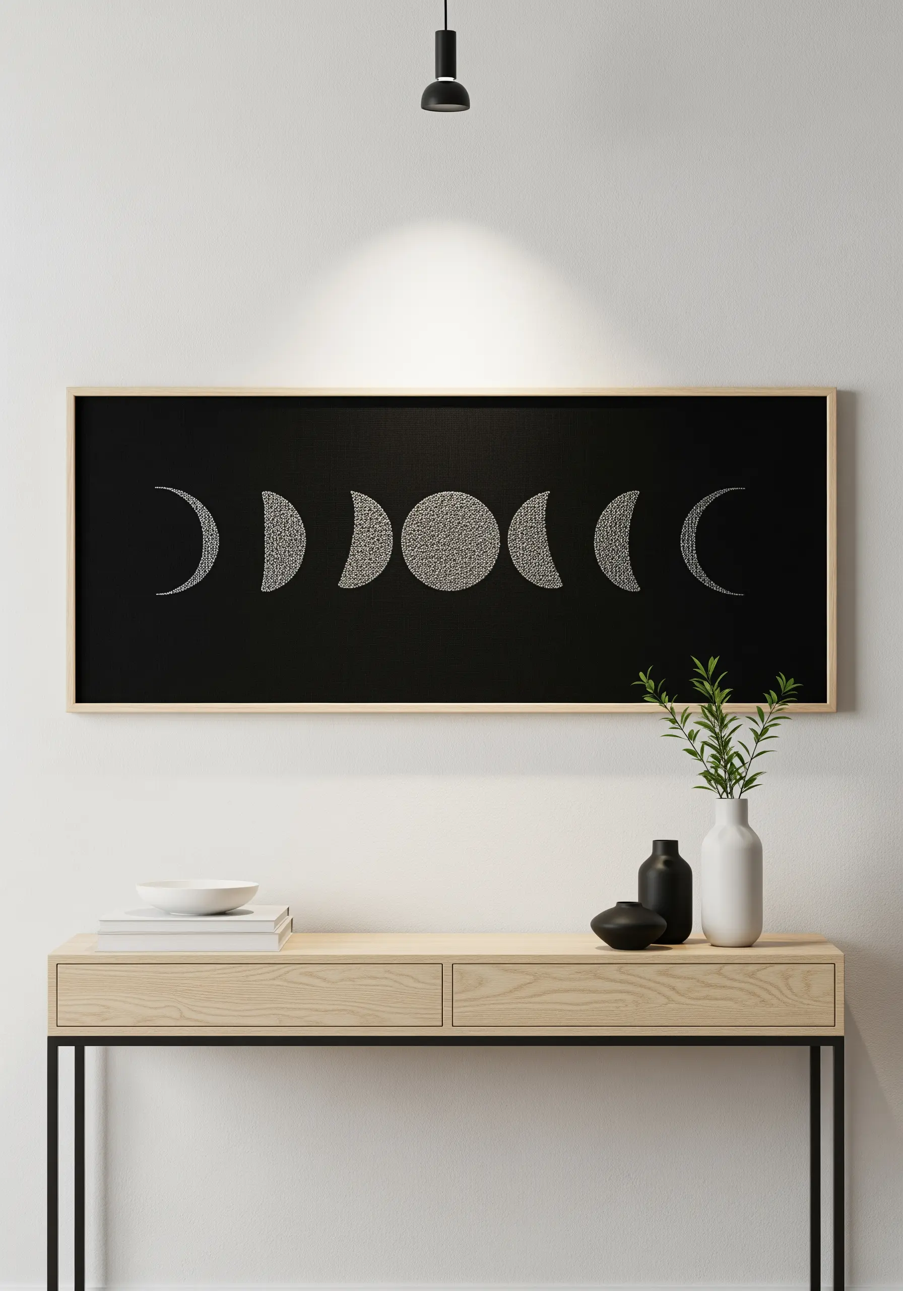 The phases of the moon stitched in white seed stitch on a long black canvas.