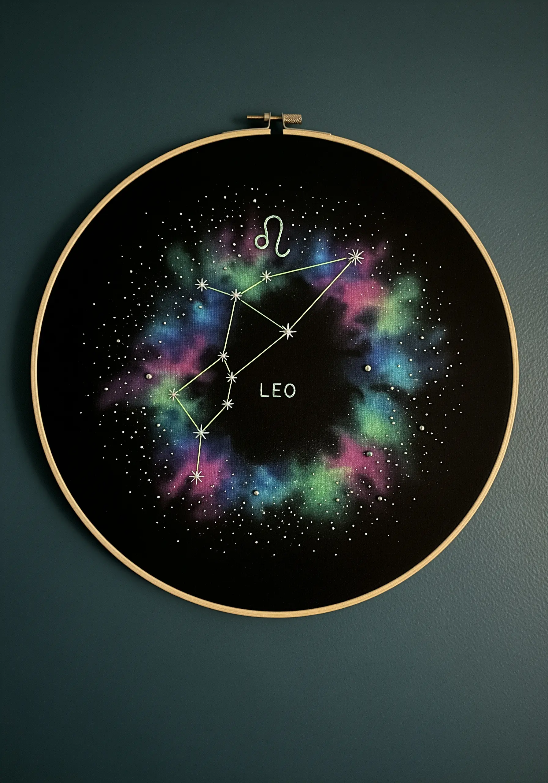 Embroidered Leo constellation on a painted galaxy background inside a black hoop.