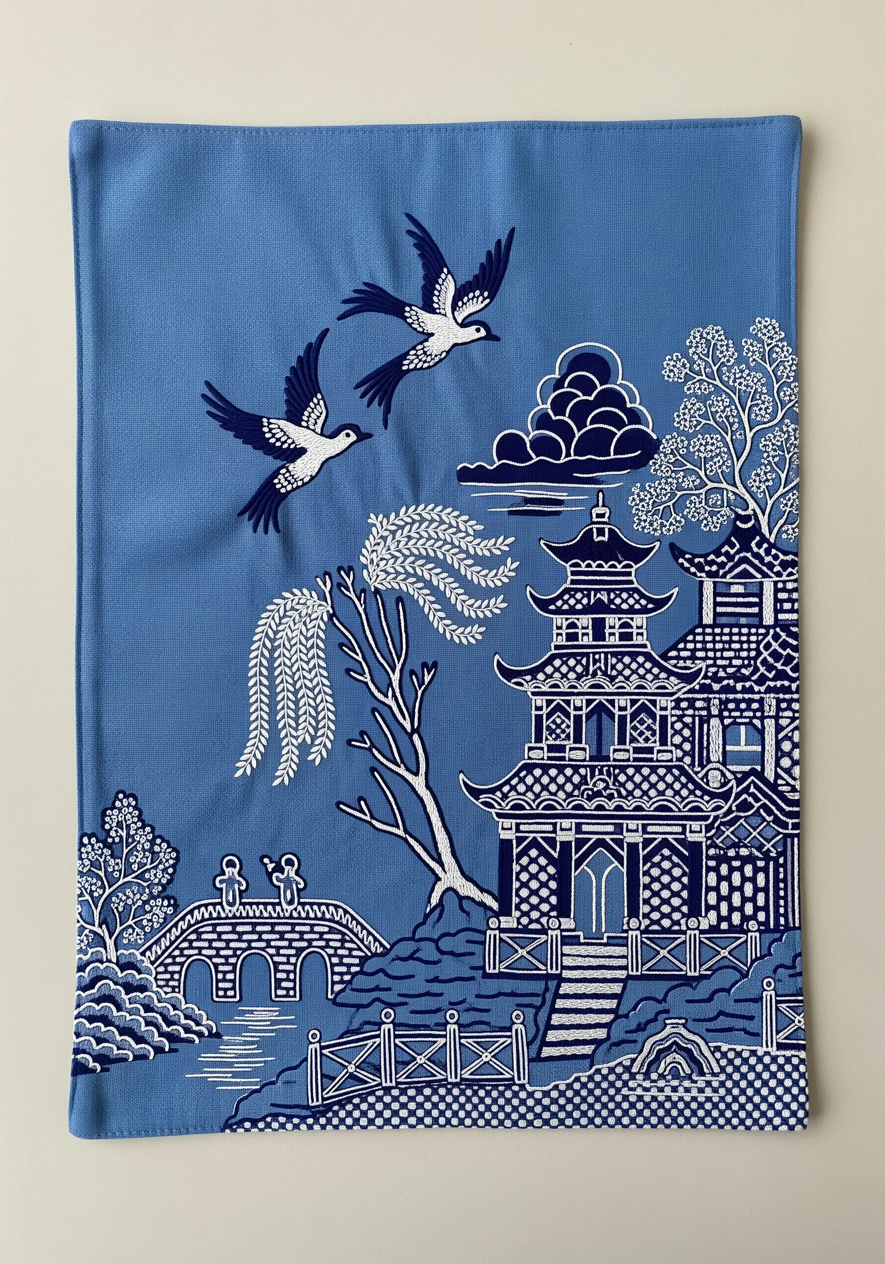 A blue and white Chinoiserie-style embroidery scene on a blue placemat.