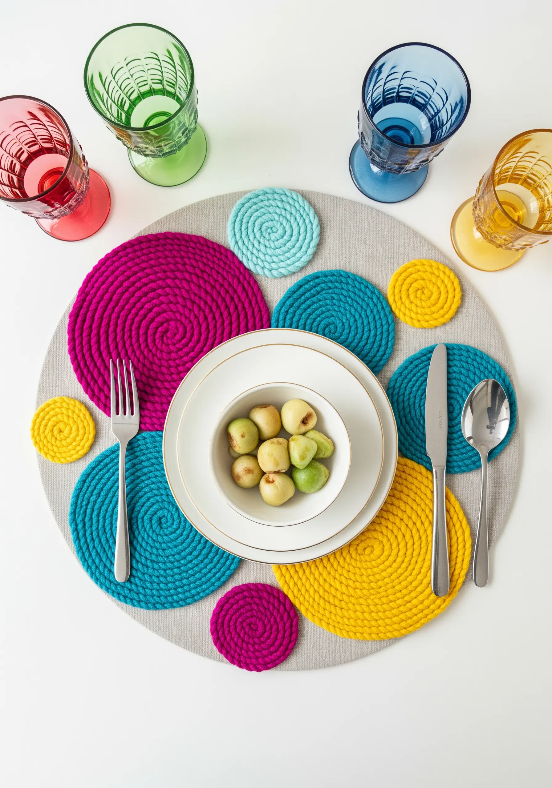 Colorful coiled yarn coasters in bright pink, yellow, and blue arranged on a placemat
