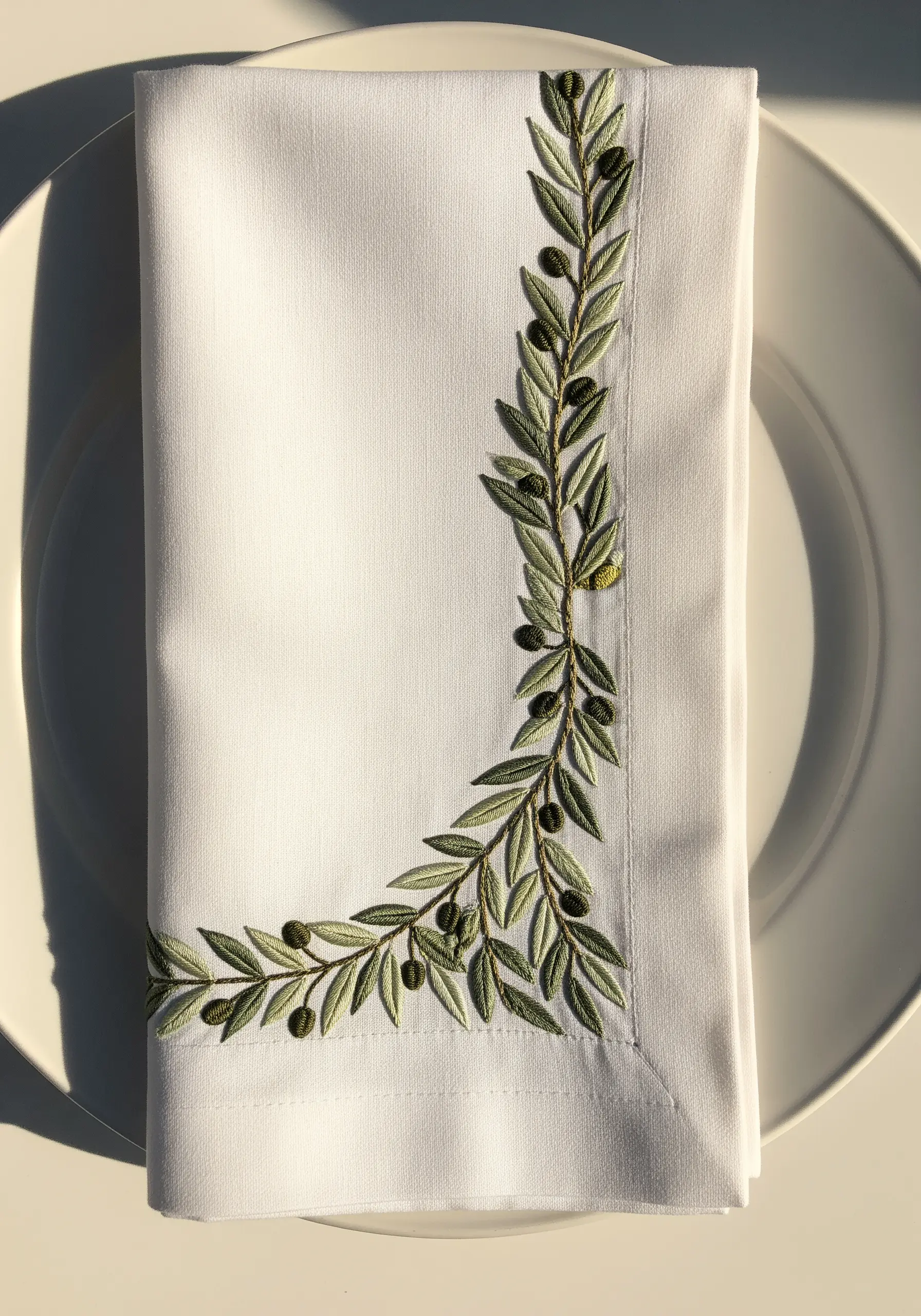 Olive branch leaf embroidery with satin stitch on the corner of a white napkin.