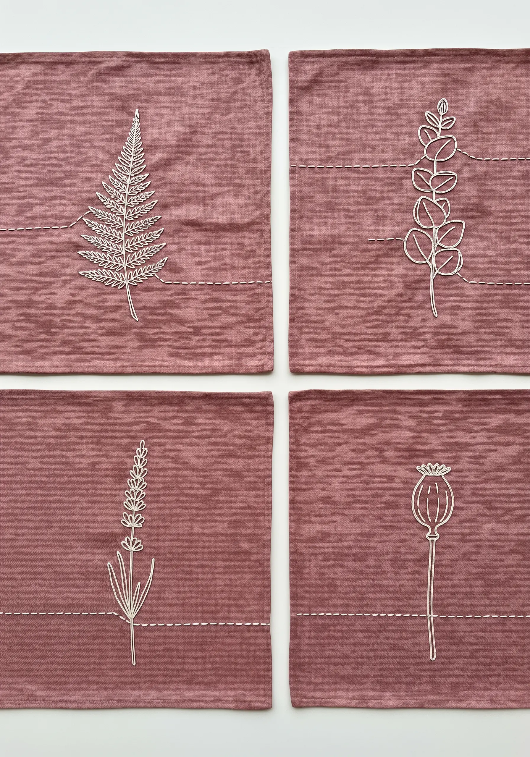 Four placemats with different white-thread botanical embroidery: fern, eucalyptus, lavender, and poppy.