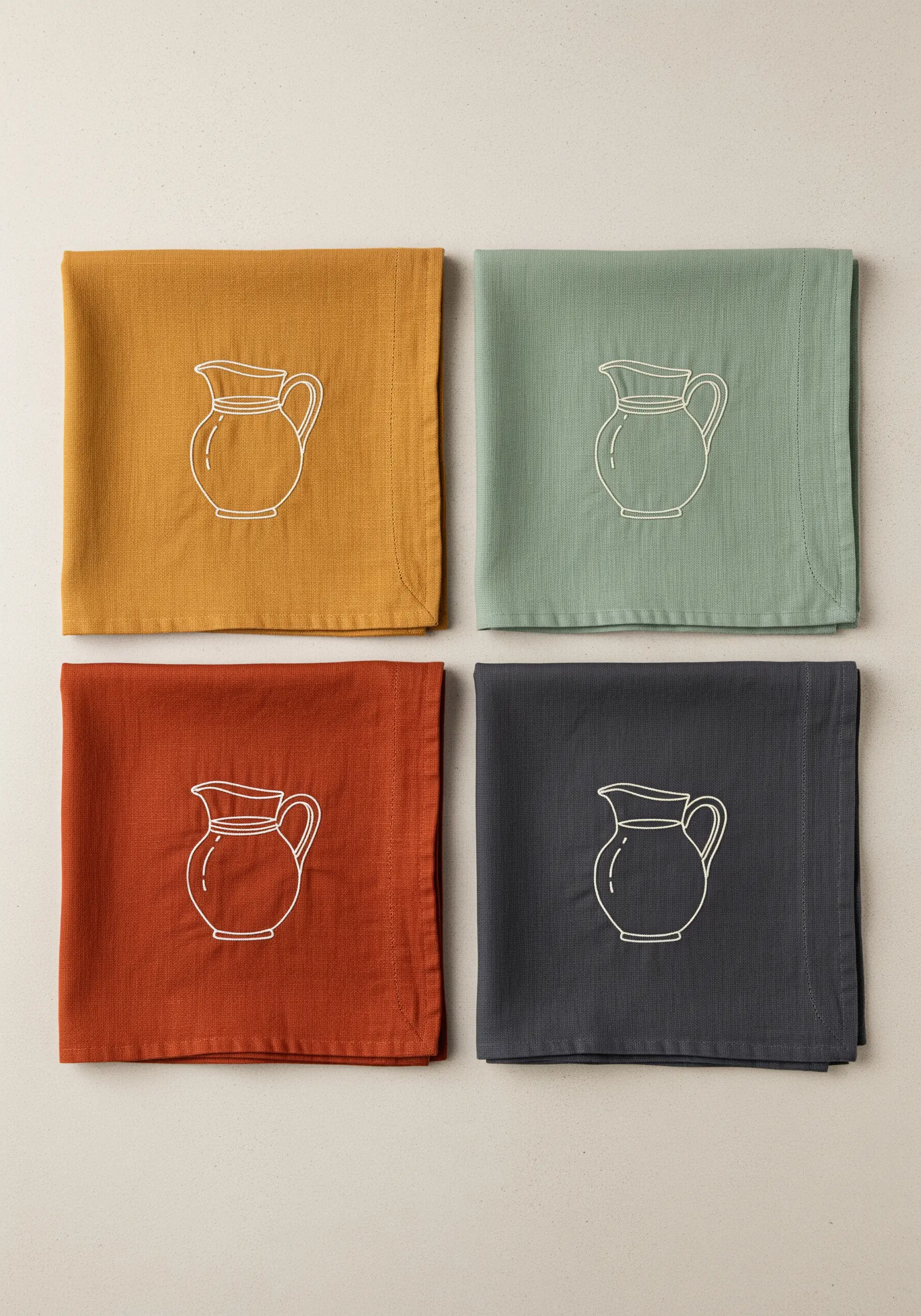 Four napkins in different colors (ochre, sage, rust, charcoal) with the same white pitcher motif.