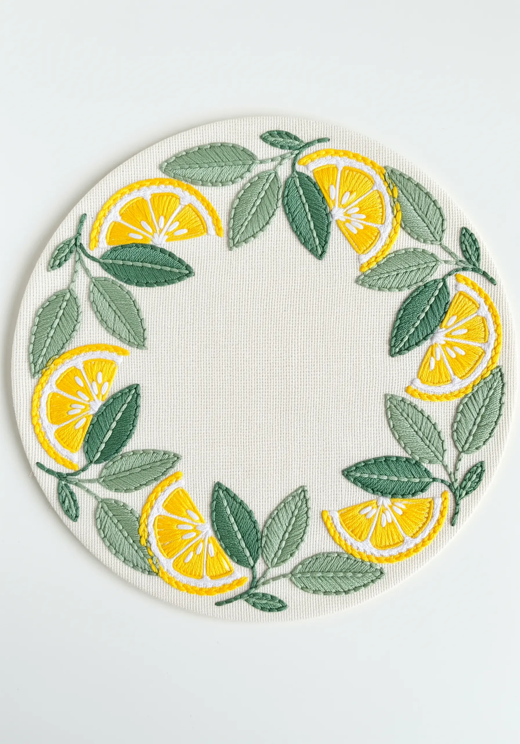 A circular placemat with a wreath of embroidered lemon slices and outlined leaves.