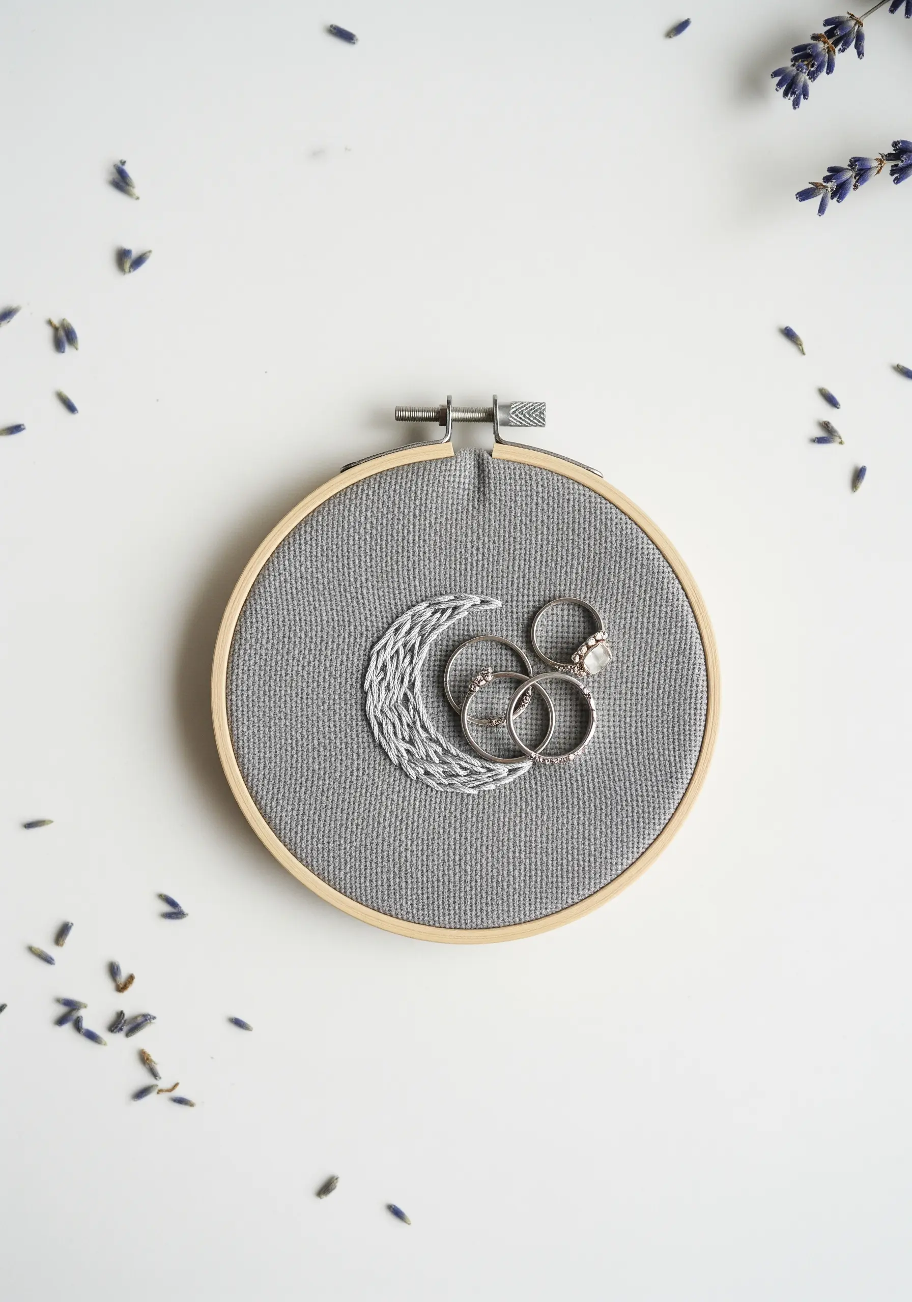 A crescent moon embroidered in silver thread, used as a ring holder in a small hoop.