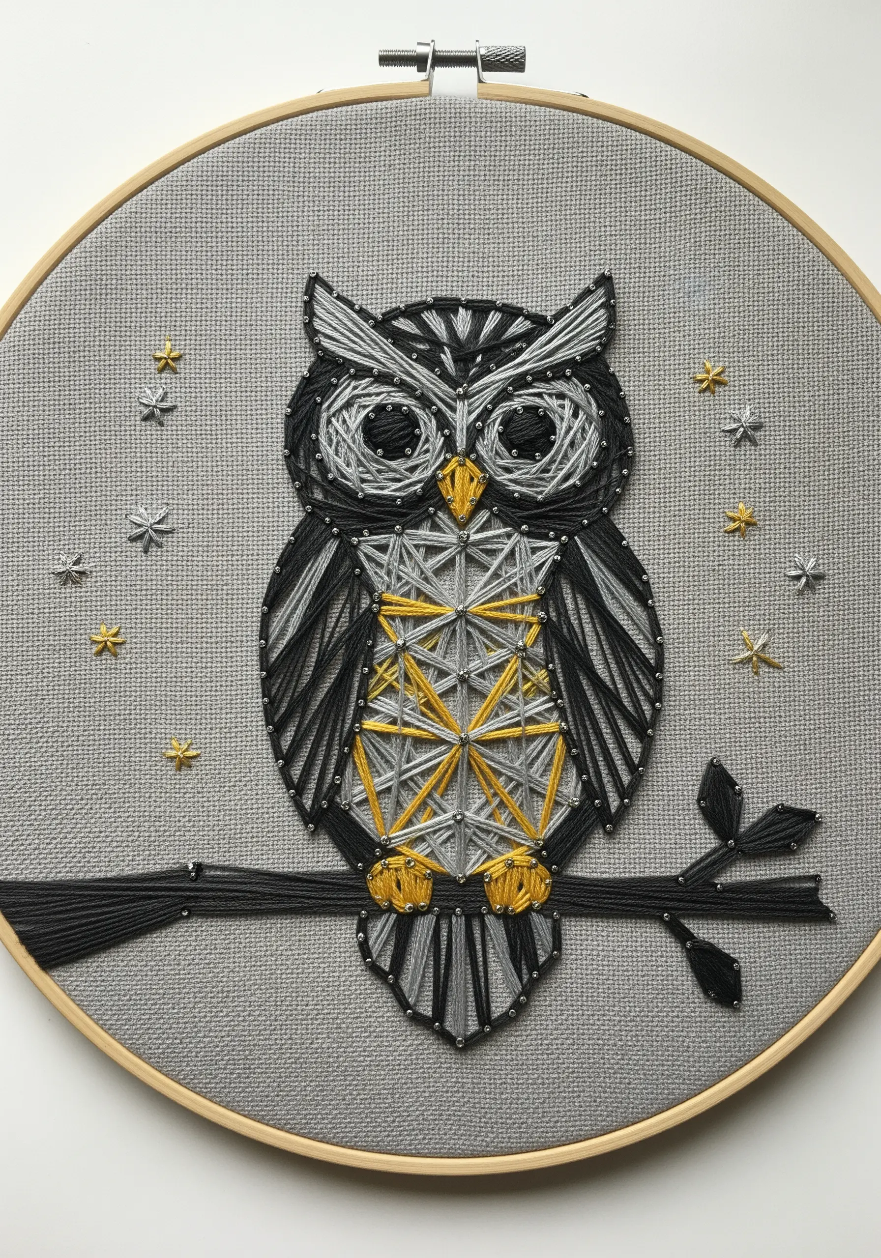 Stylized owl embroidery with geometric patterns in black, grey, and gold thread.