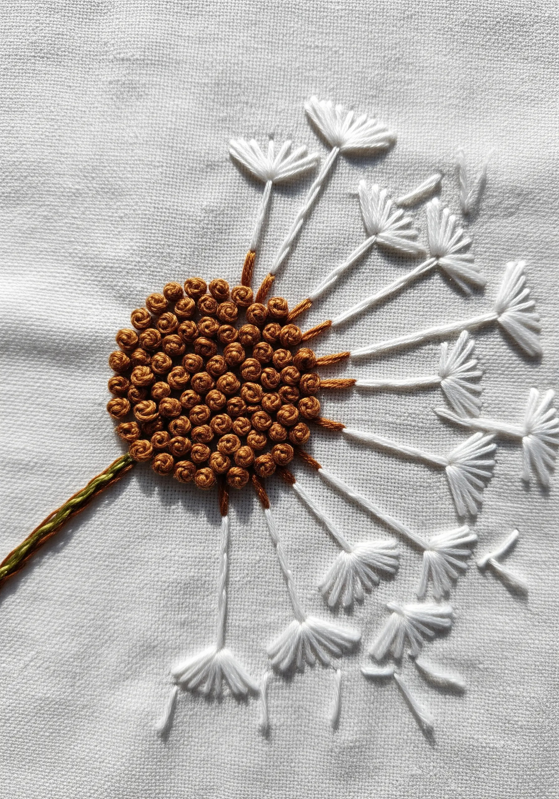 Embroidered dandelion with a textured French knot center and flying white seeds.