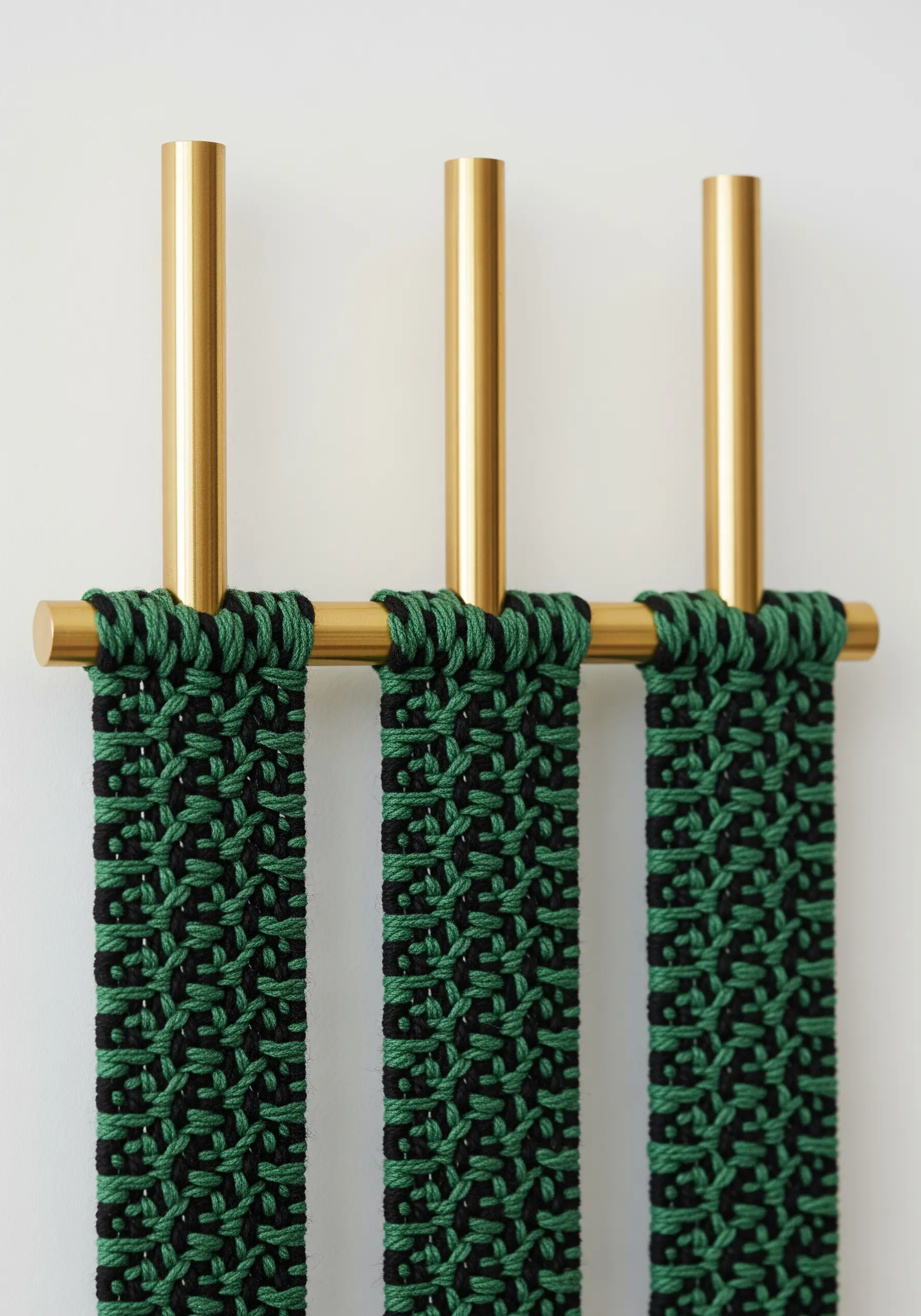 Modern macrame strips in black and green hanging from a polished brass wall fixture.