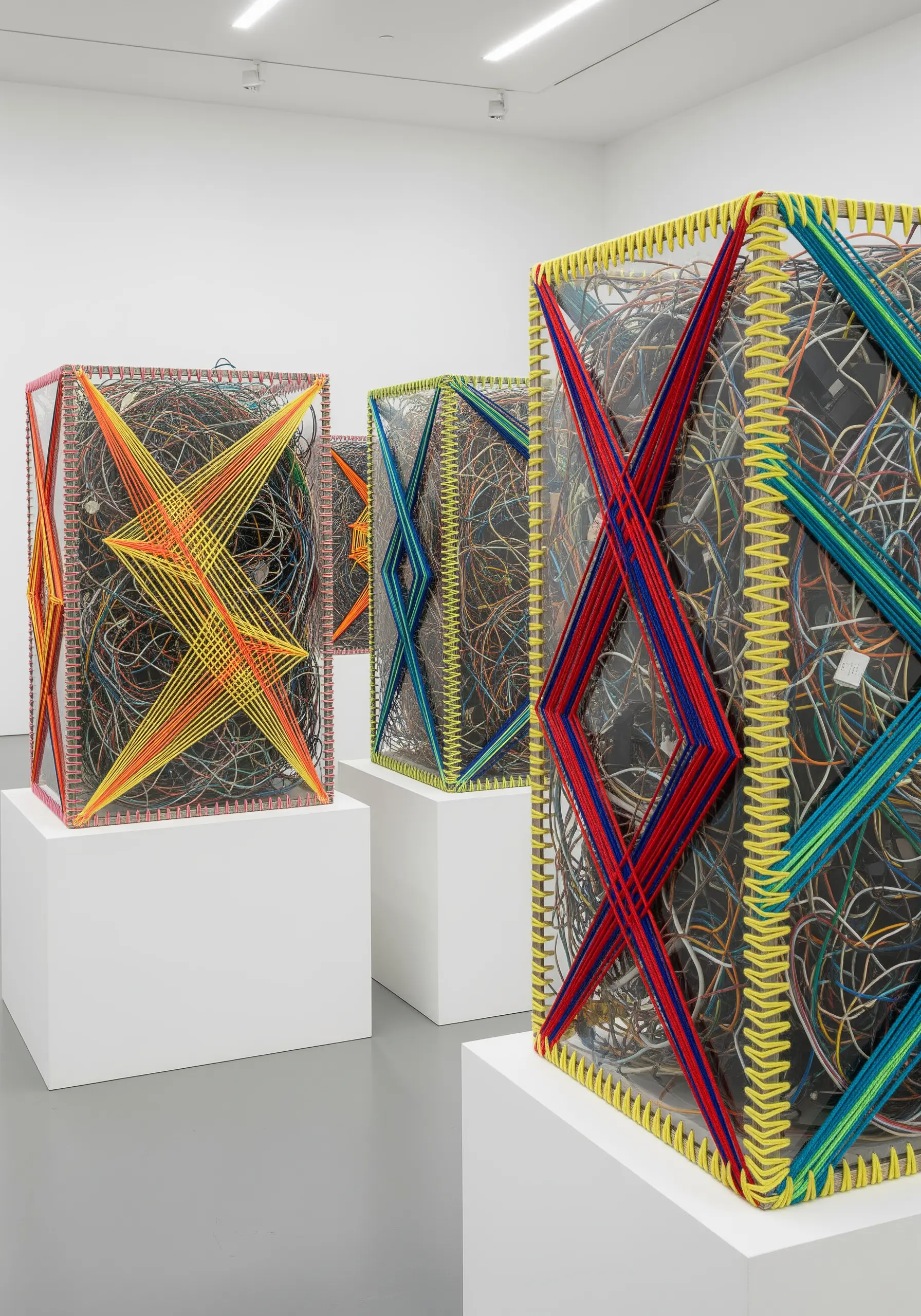 Geometric sculptures made of clear boxes filled with tangled wires and wrapped in colorful thread.