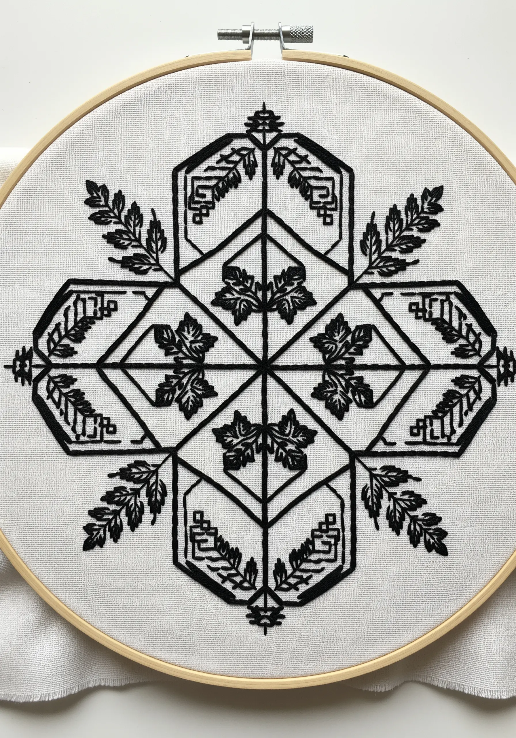 A blackwork embroidery design in a hoop, featuring geometric patterns mixed with leaf motifs.