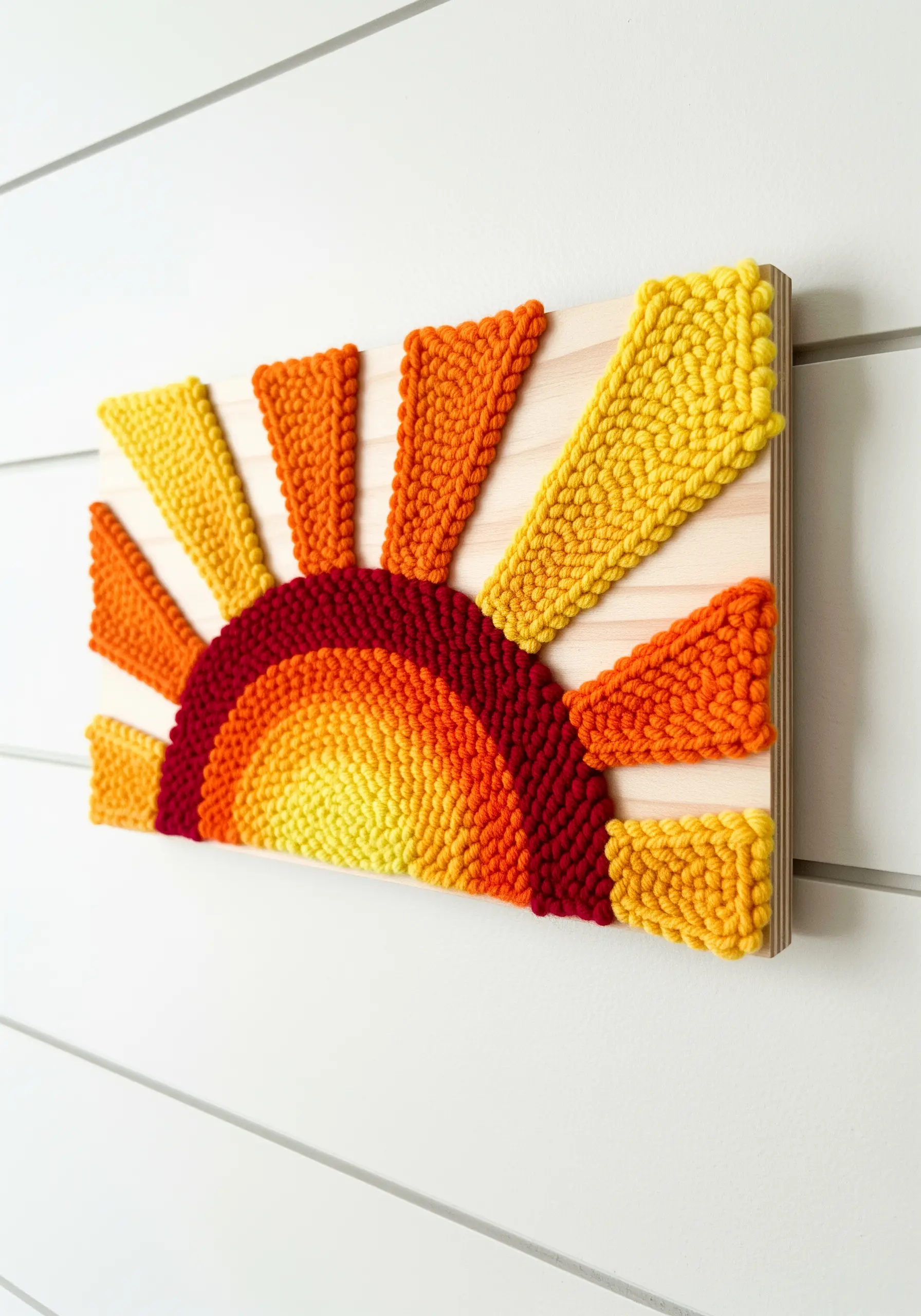 A punch needle sun with orange and yellow rays, mounted on a light wood panel.