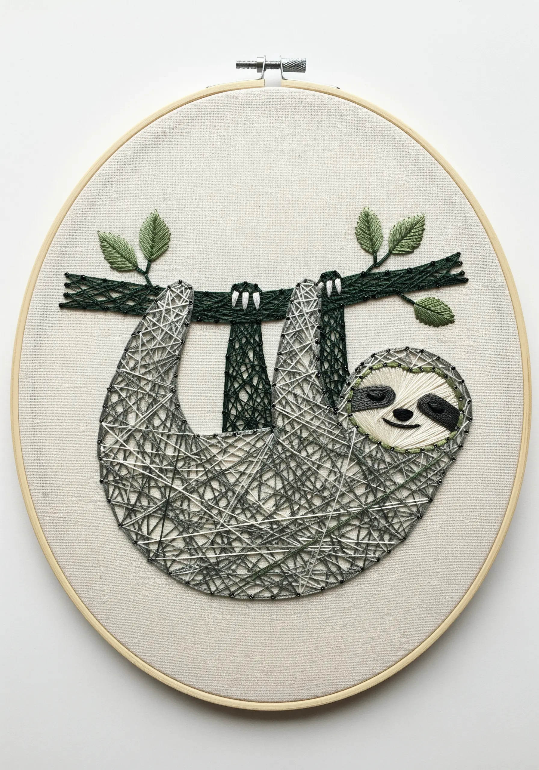 Embroidered sloth hanging from a branch, stitched in grey, green, and brown threads.