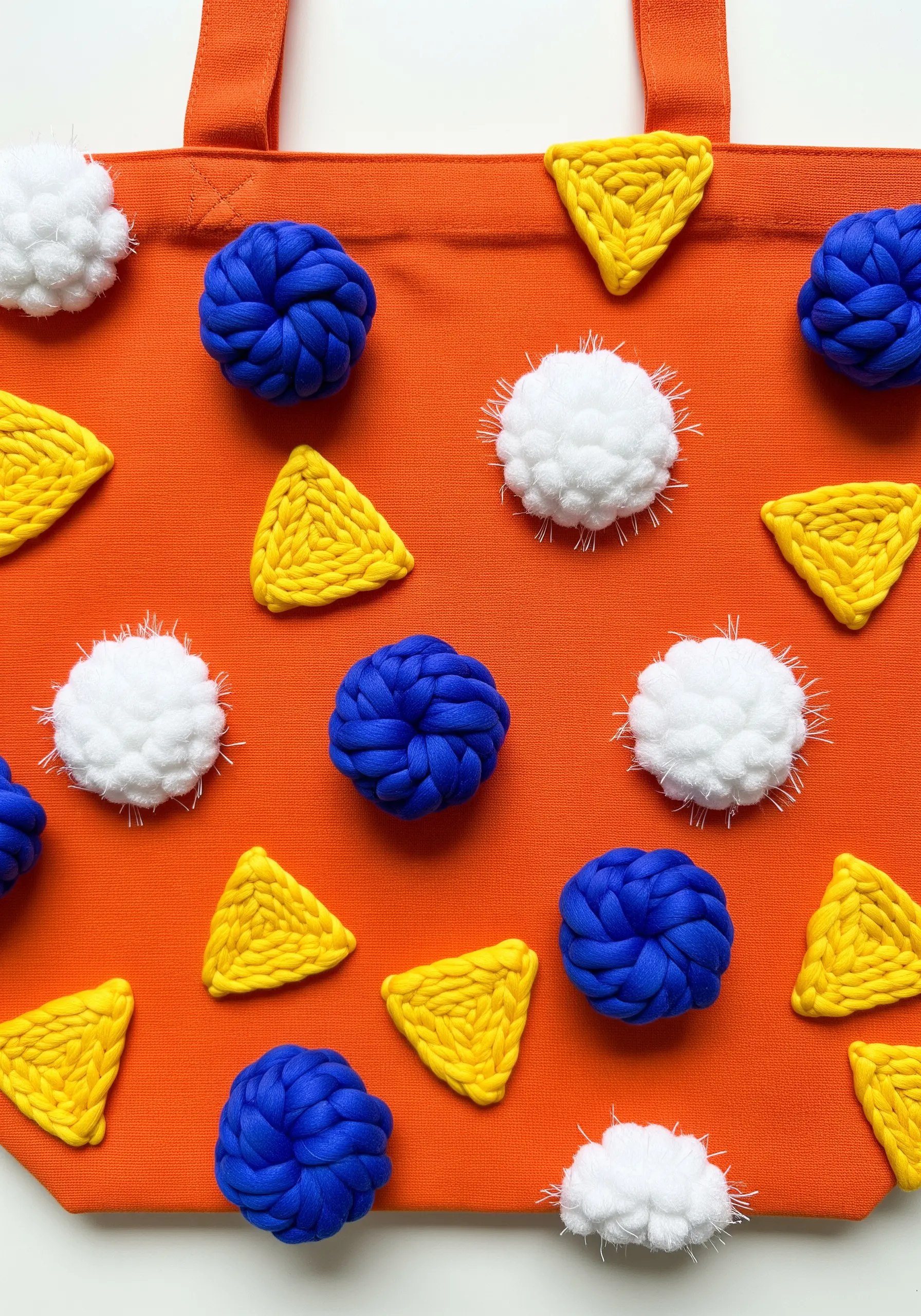 Abstract woven shapes in blue, yellow, and white on a bright orange tote bag.