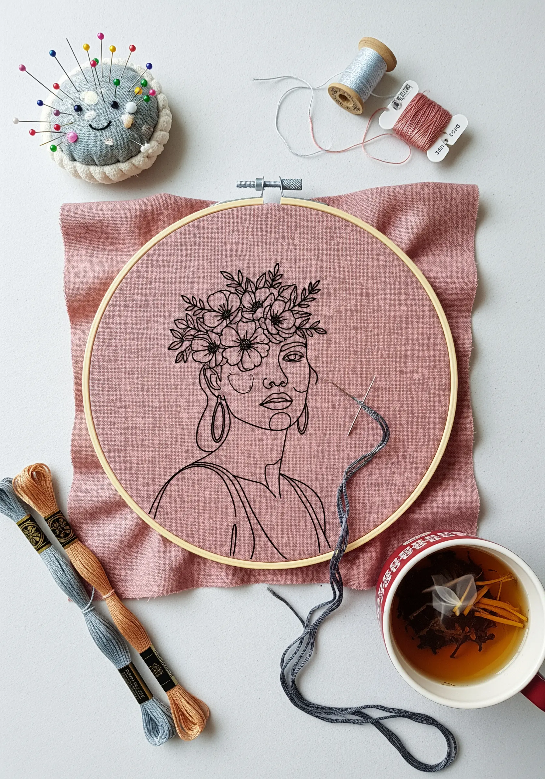 Line-art portrait with a detailed floral crown embroidered in an embroidery hoop.