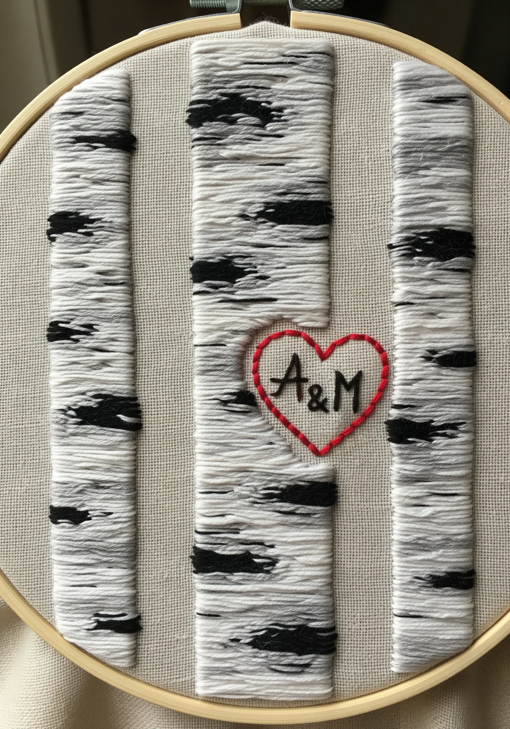 Embroidery of three birch tree trunks with a red heart and initials carved into one.