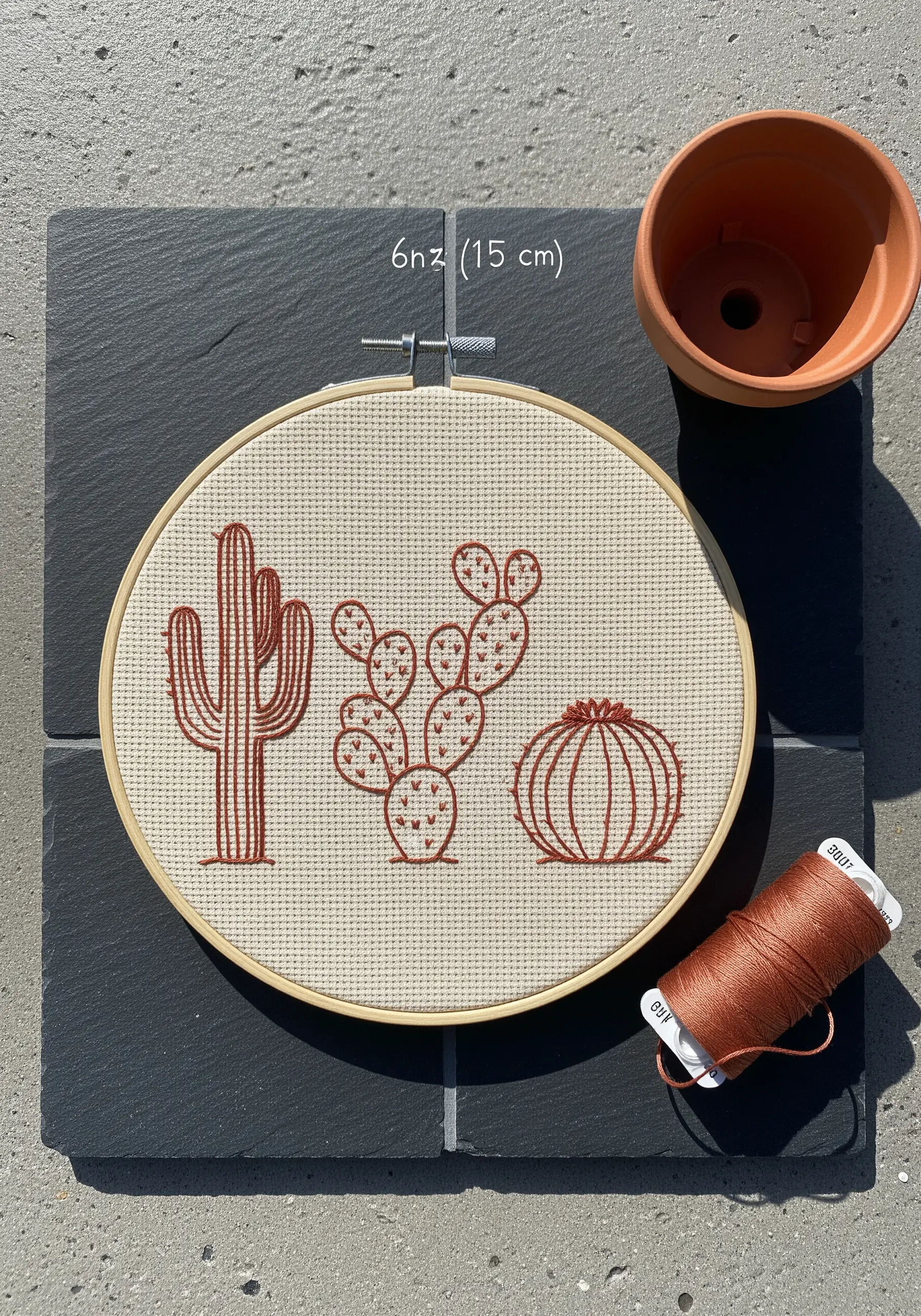 Three different cacti embroidered in terracotta thread on off-white Aida cloth in a hoop.