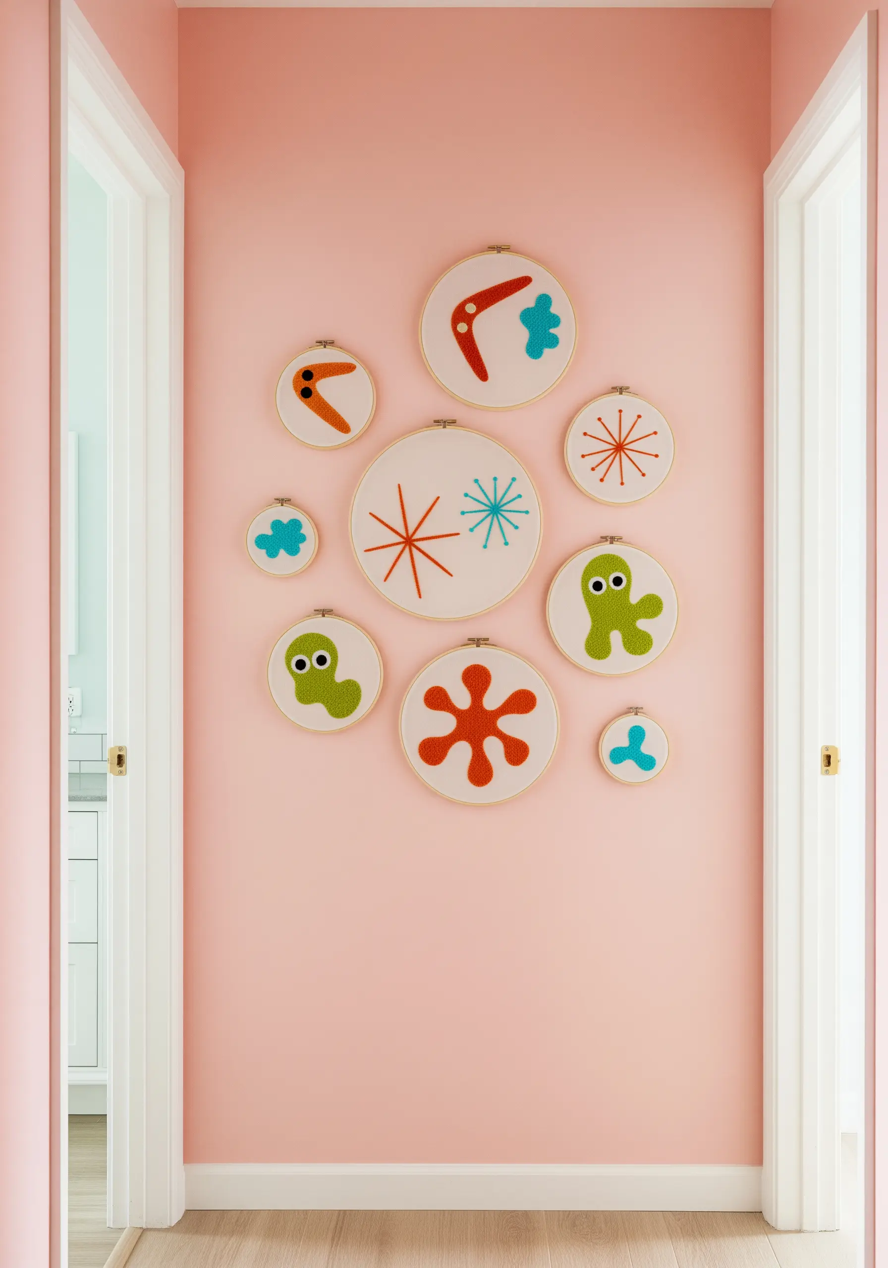 A playful gallery wall of embroidery hoops with colorful, retro abstract shapes on a pink wall.