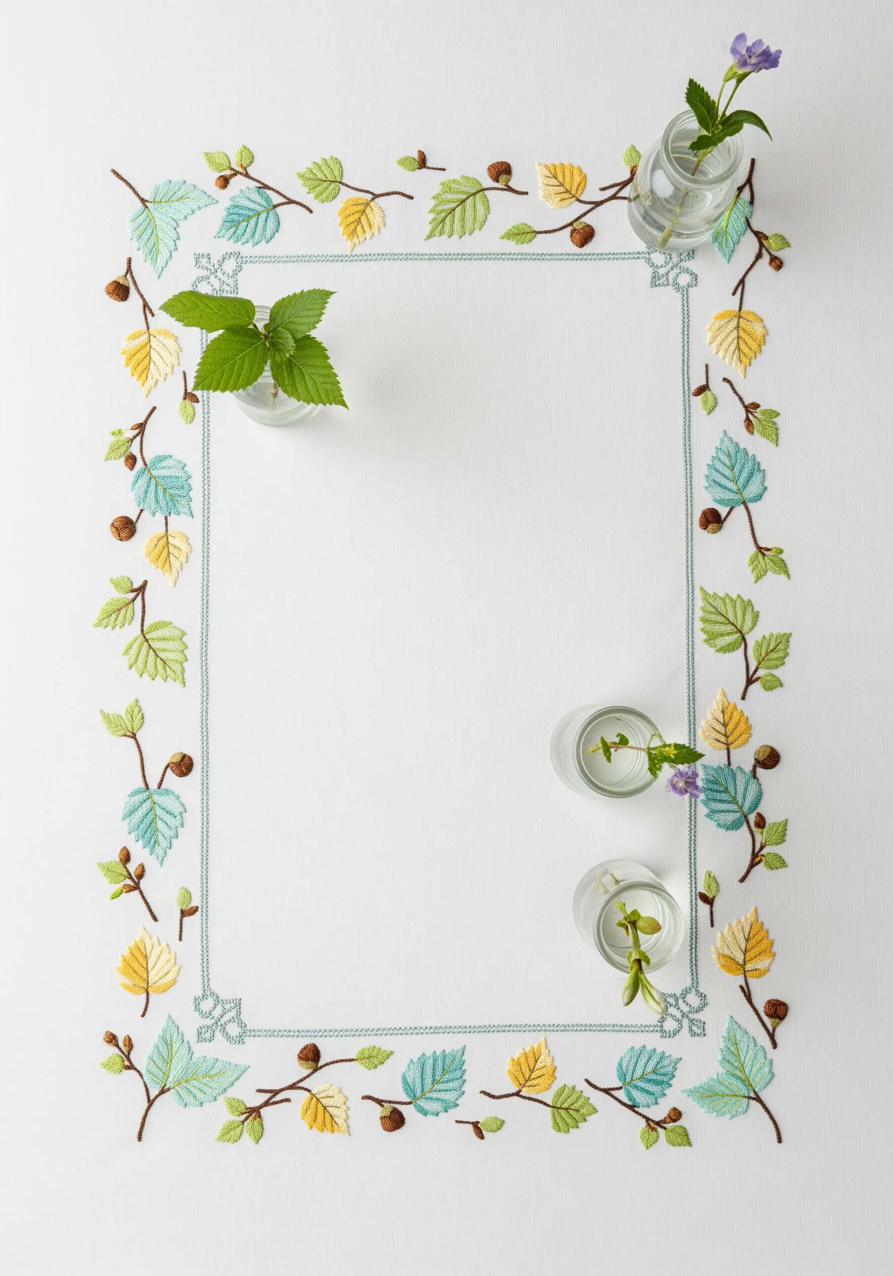 A rectangular border of small, delicate leaves in blue, green, and yellow on a white cloth.