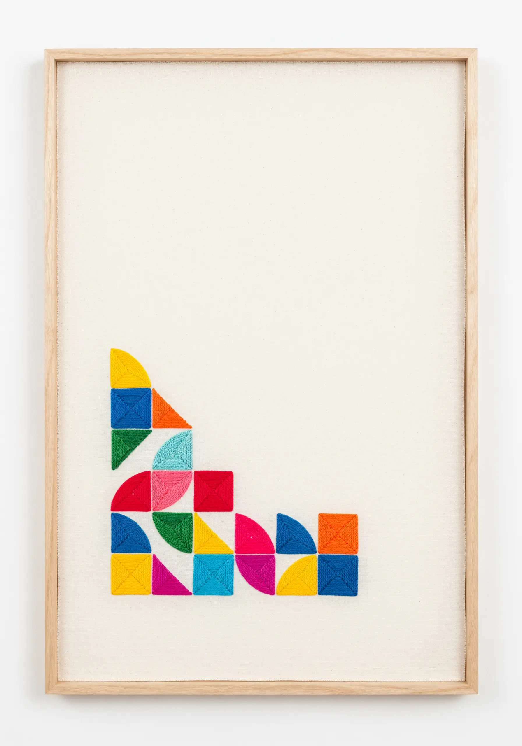 Minimalist embroidery with small, colorful geometric shapes clustered in the bottom corner of a framed canvas.