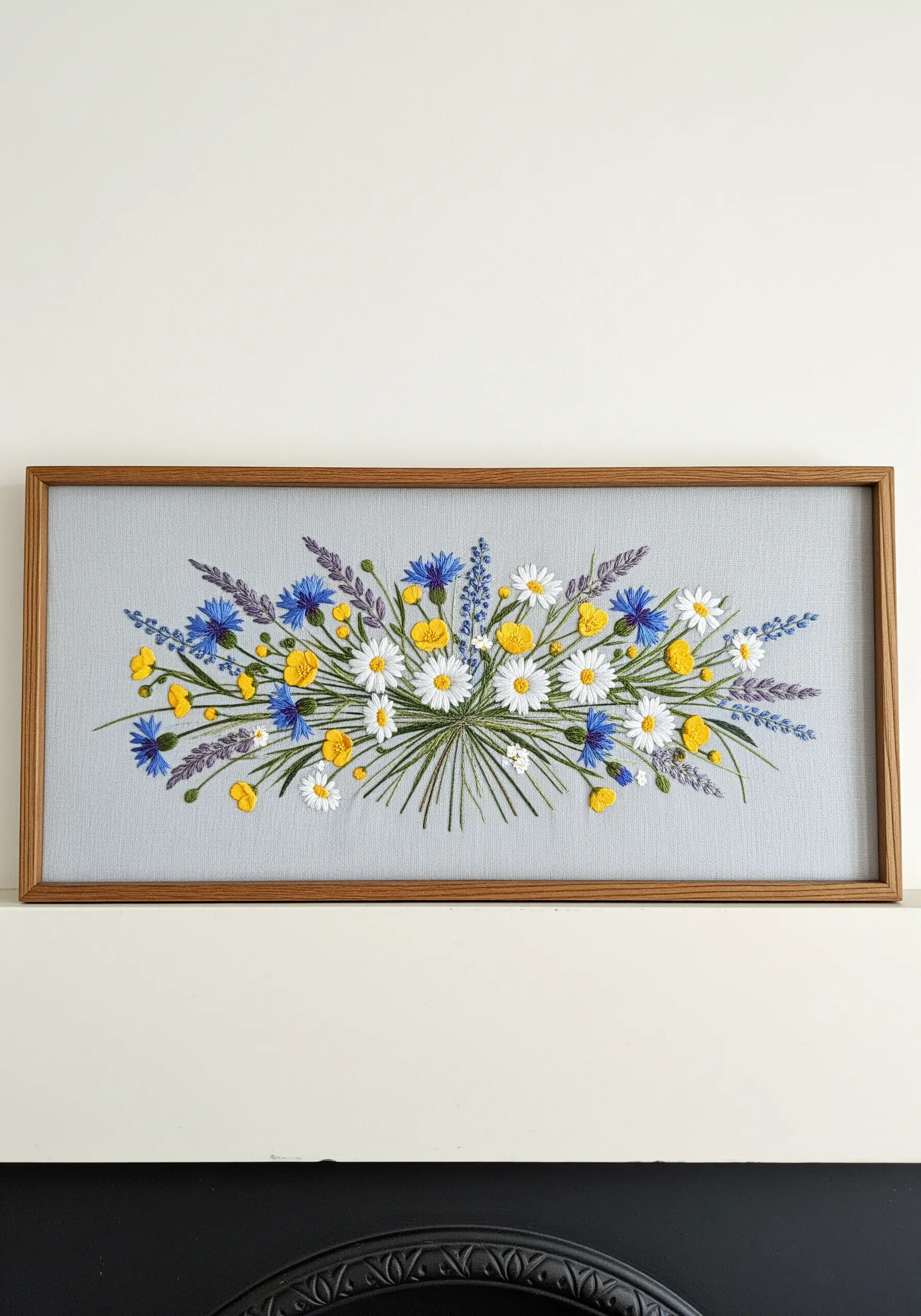 A panoramic framed embroidery of a wildflower bouquet with daisies and cornflowers.