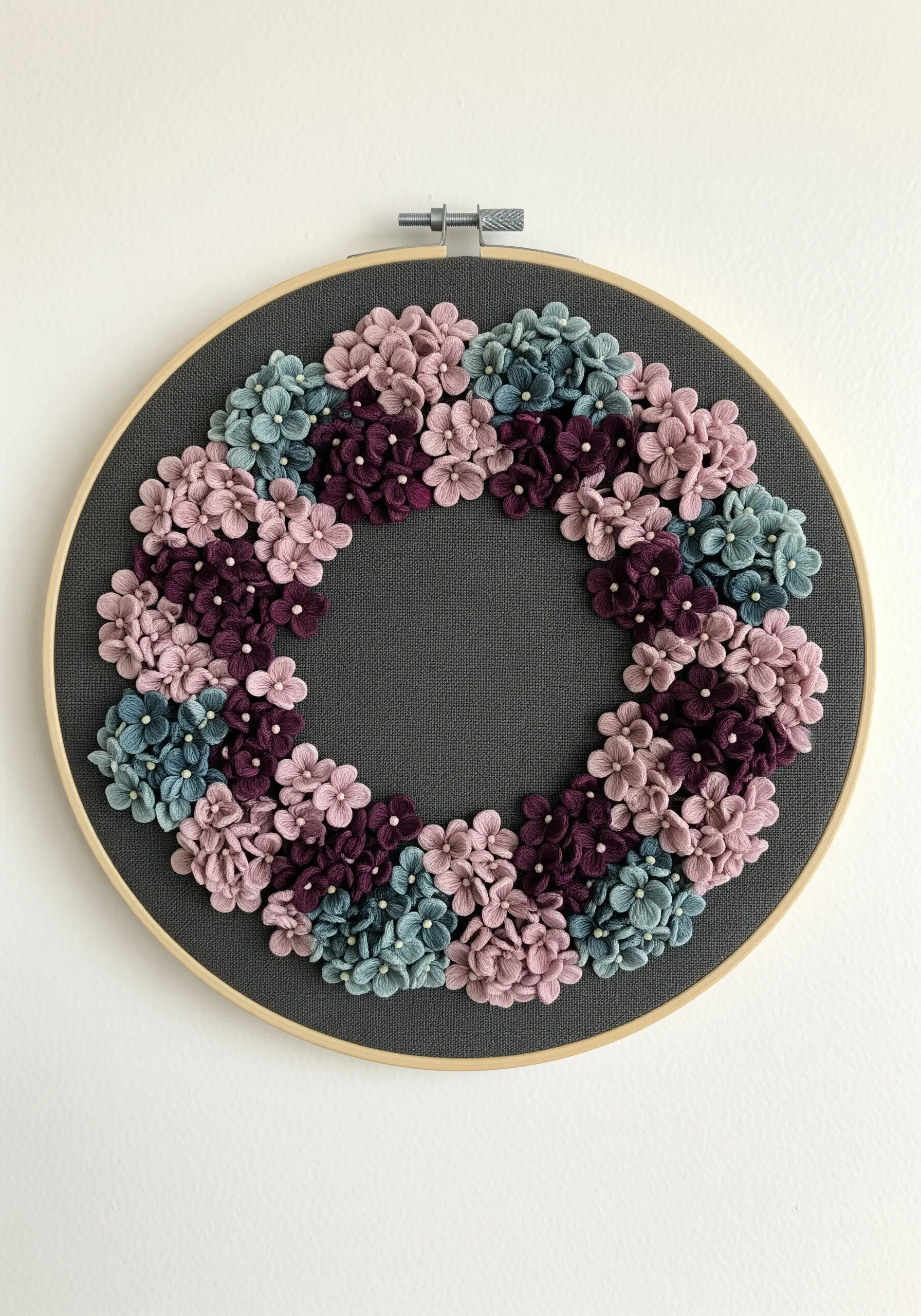 A floral wreath of mauve, teal, and purple hydrangeas on dark grey fabric.