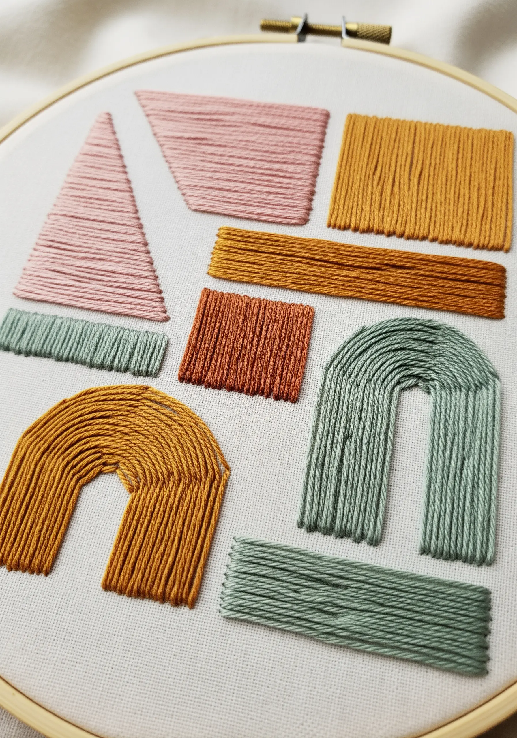 A collection of abstract geometric shapes filled with satin stitch in earthy tones.