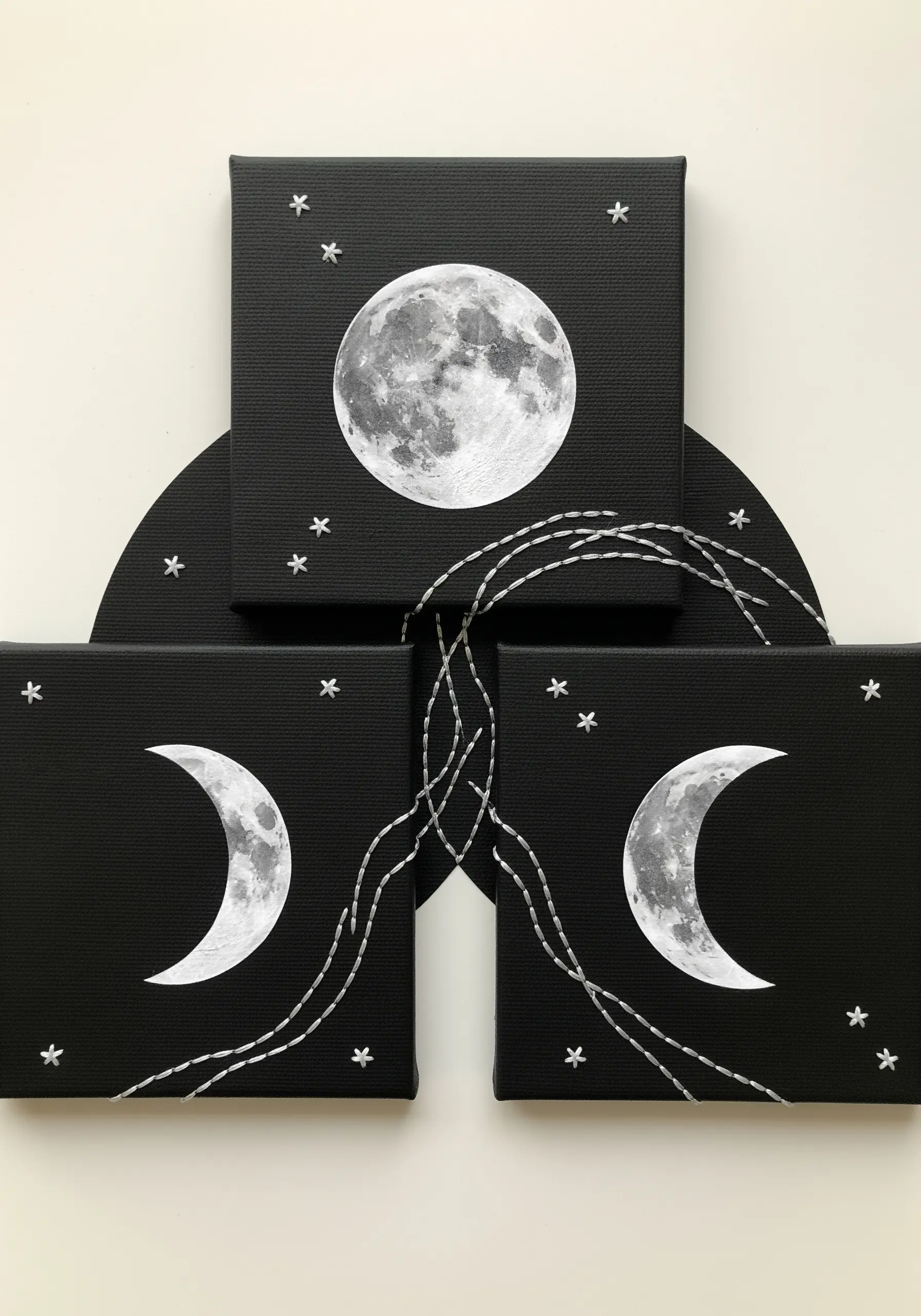 Three small black canvases depicting moon phases, connected by flowing white stitched lines.