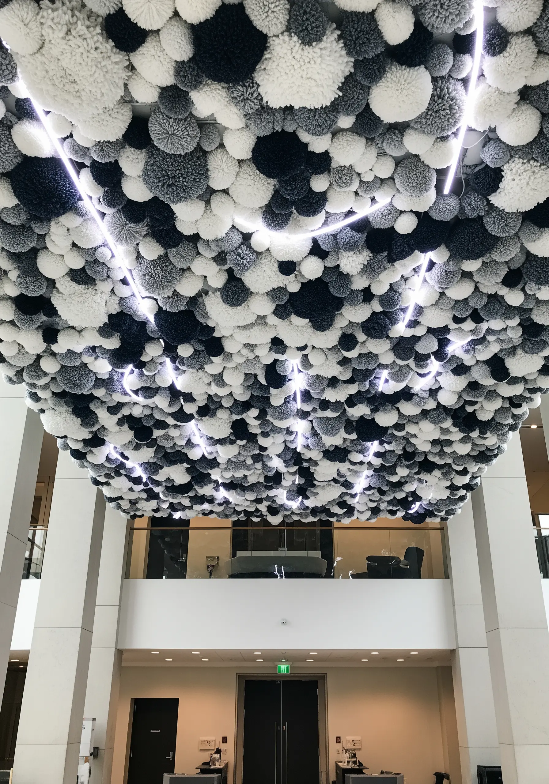 A ceiling covered in a dense cloud of black, white, and grey yarn pom-poms.