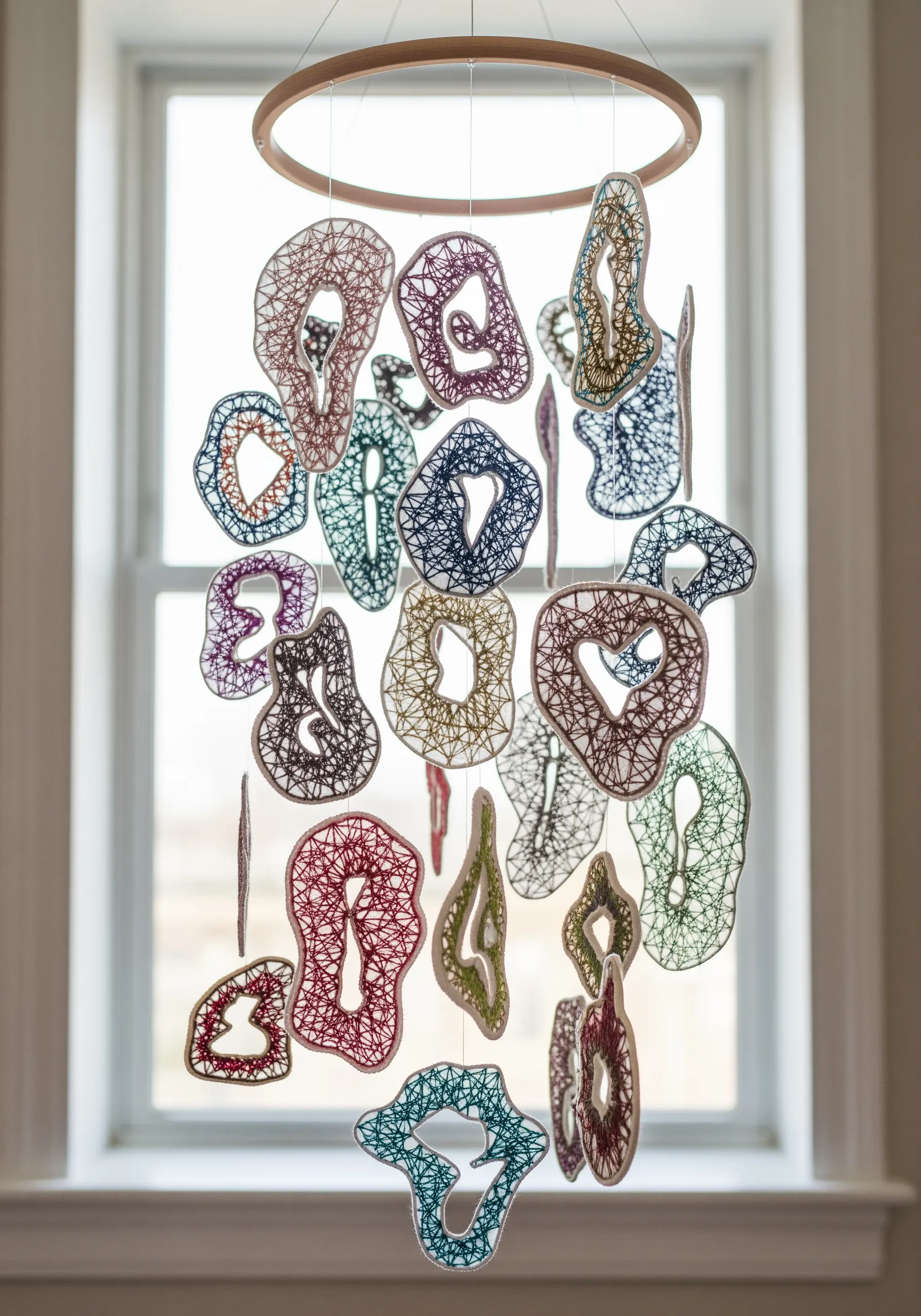 A colorful mobile made of many small, organic thread-wrapped forms hanging from a hoop.