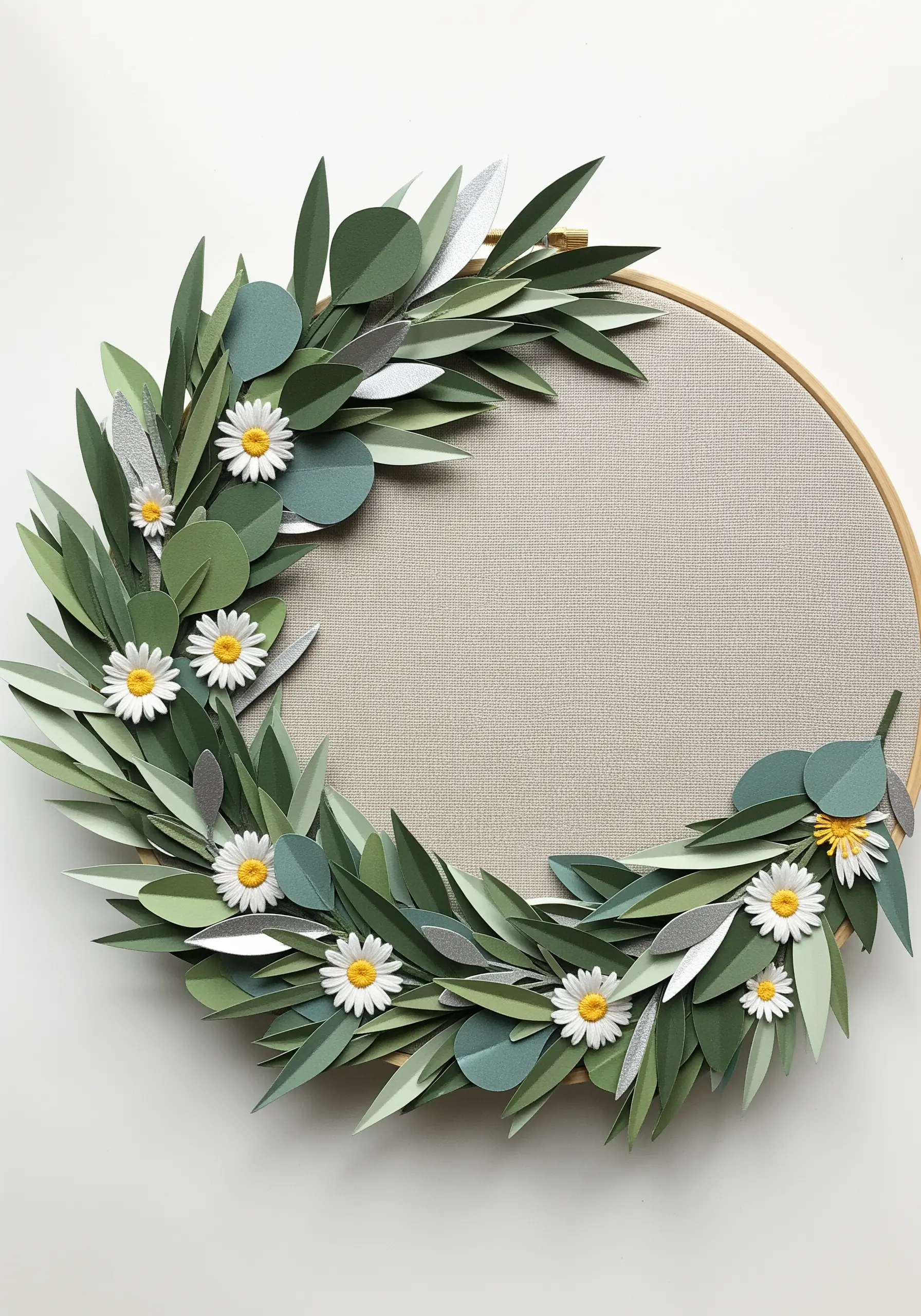 An embroidery hoop filled with a wreath made from layered green and silver paper leaves and small daisies.