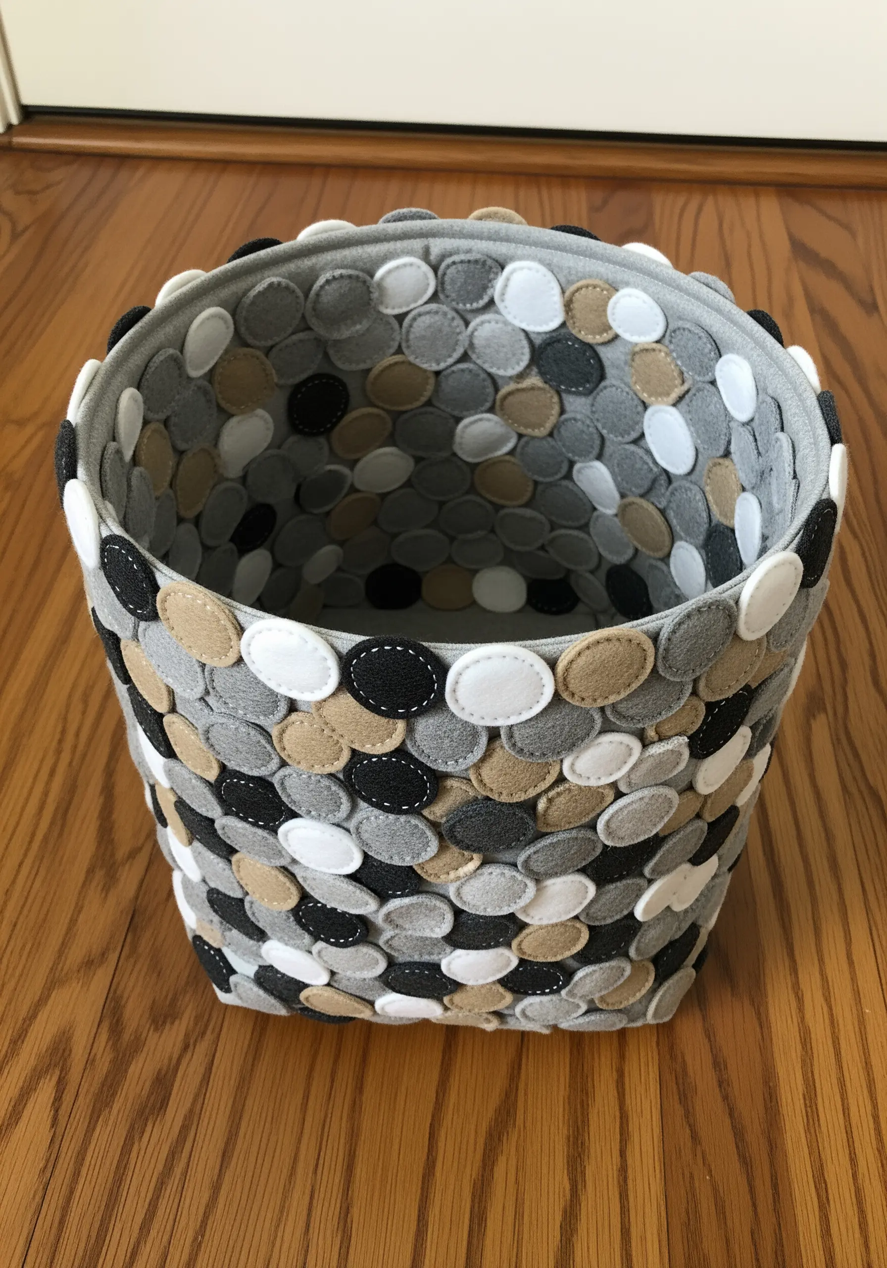 A fabric basket covered in overlapping, stitched-on felt circles in neutral colors.