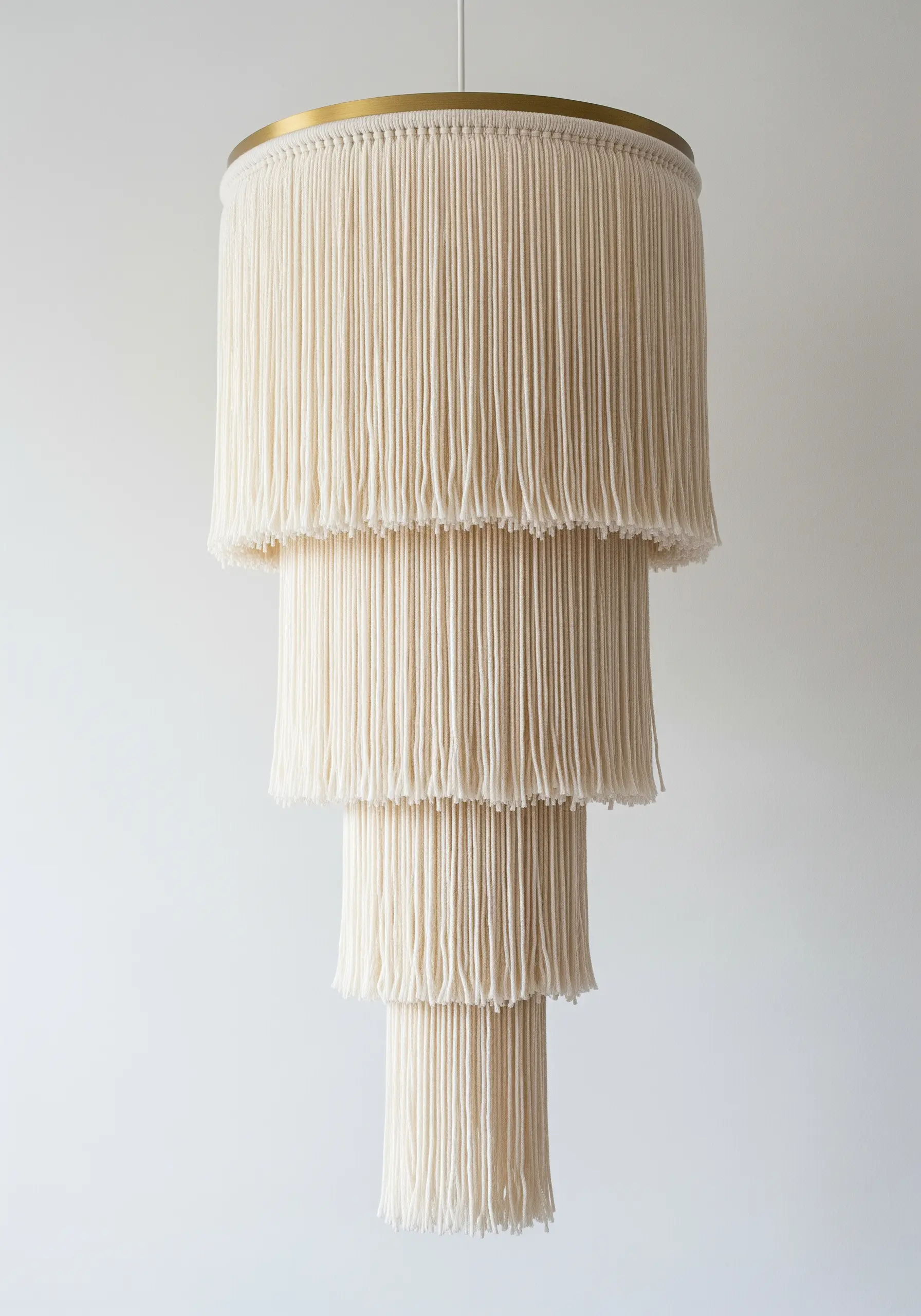 A tiered macrame-style chandelier made of white yarn fringe hanging from brass rings.