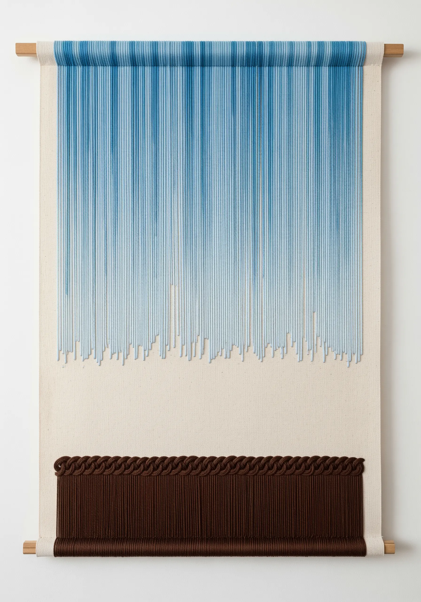 A wall hanging with a gradient of blue threads hanging vertically over a band of brown texture.