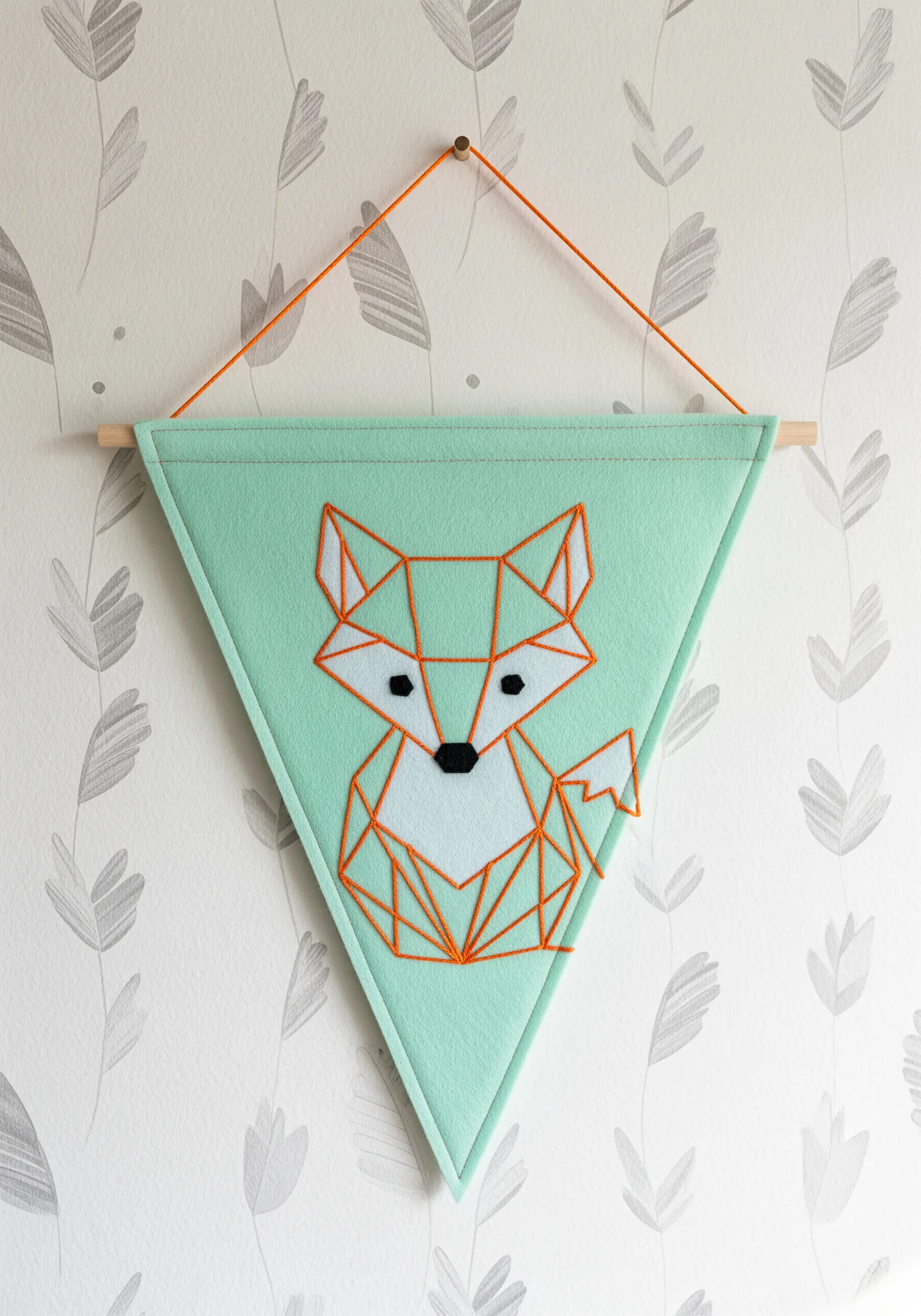 A geometric fox made of orange straight stitches on a mint green felt pennant.