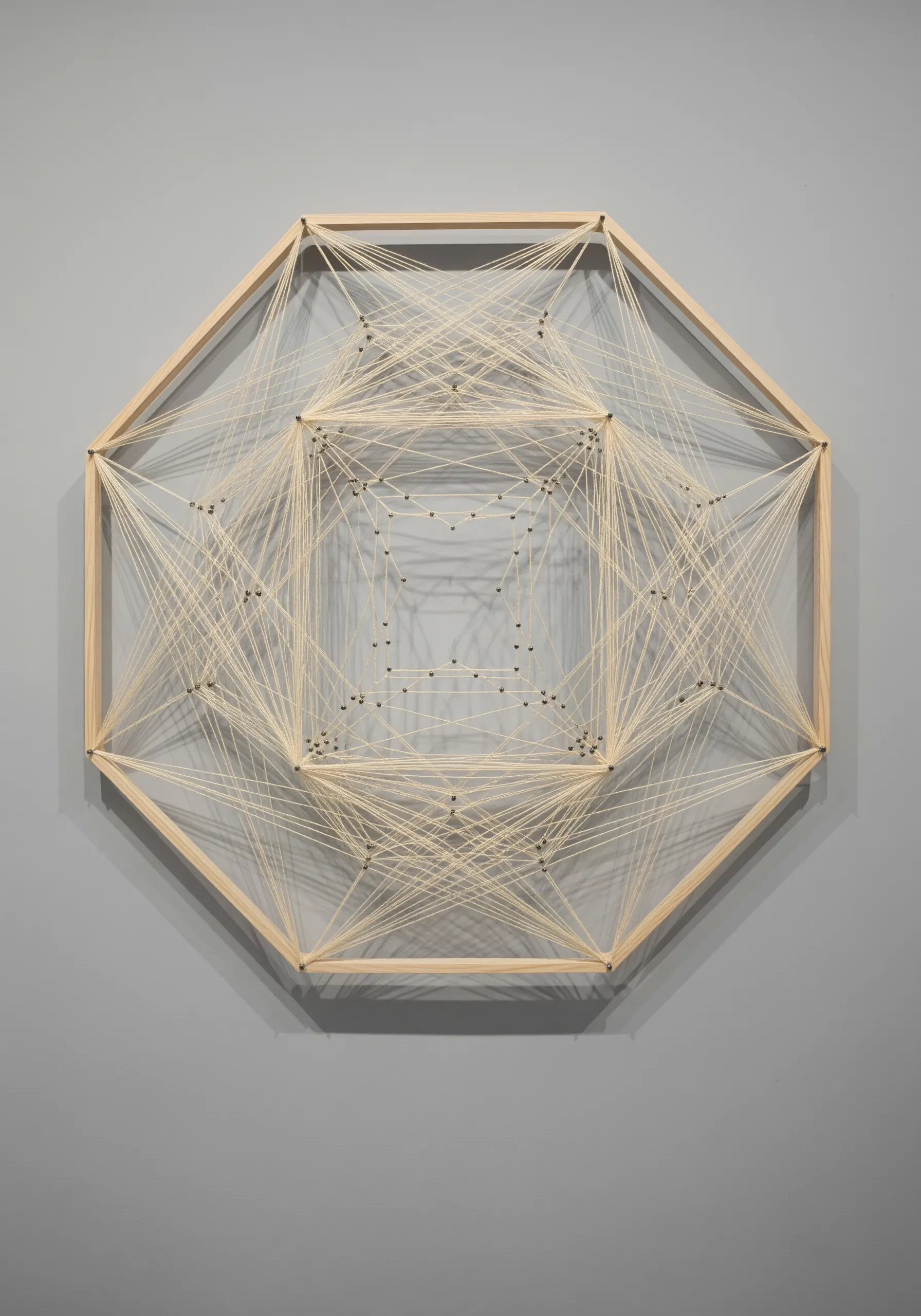 An octagonal wooden frame with cream-colored string woven between nails to form geometric layers.