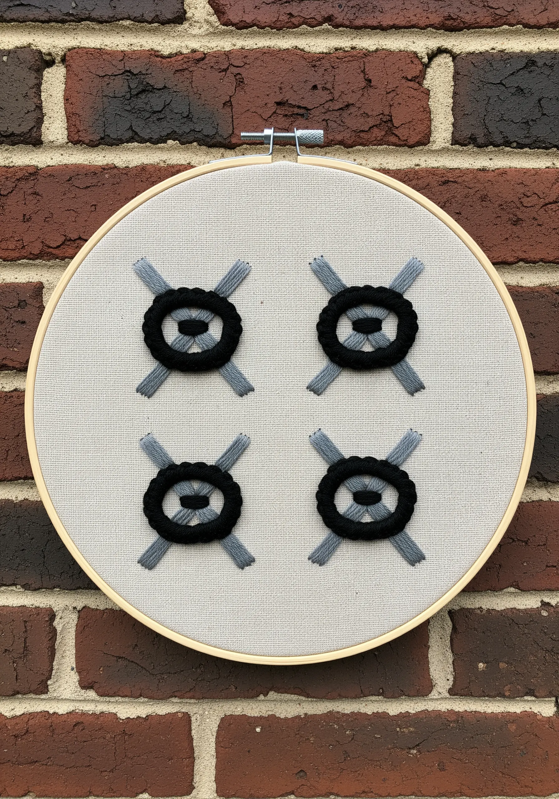 Four geometric motifs embroidered with woven black thread over gray straight stitches.