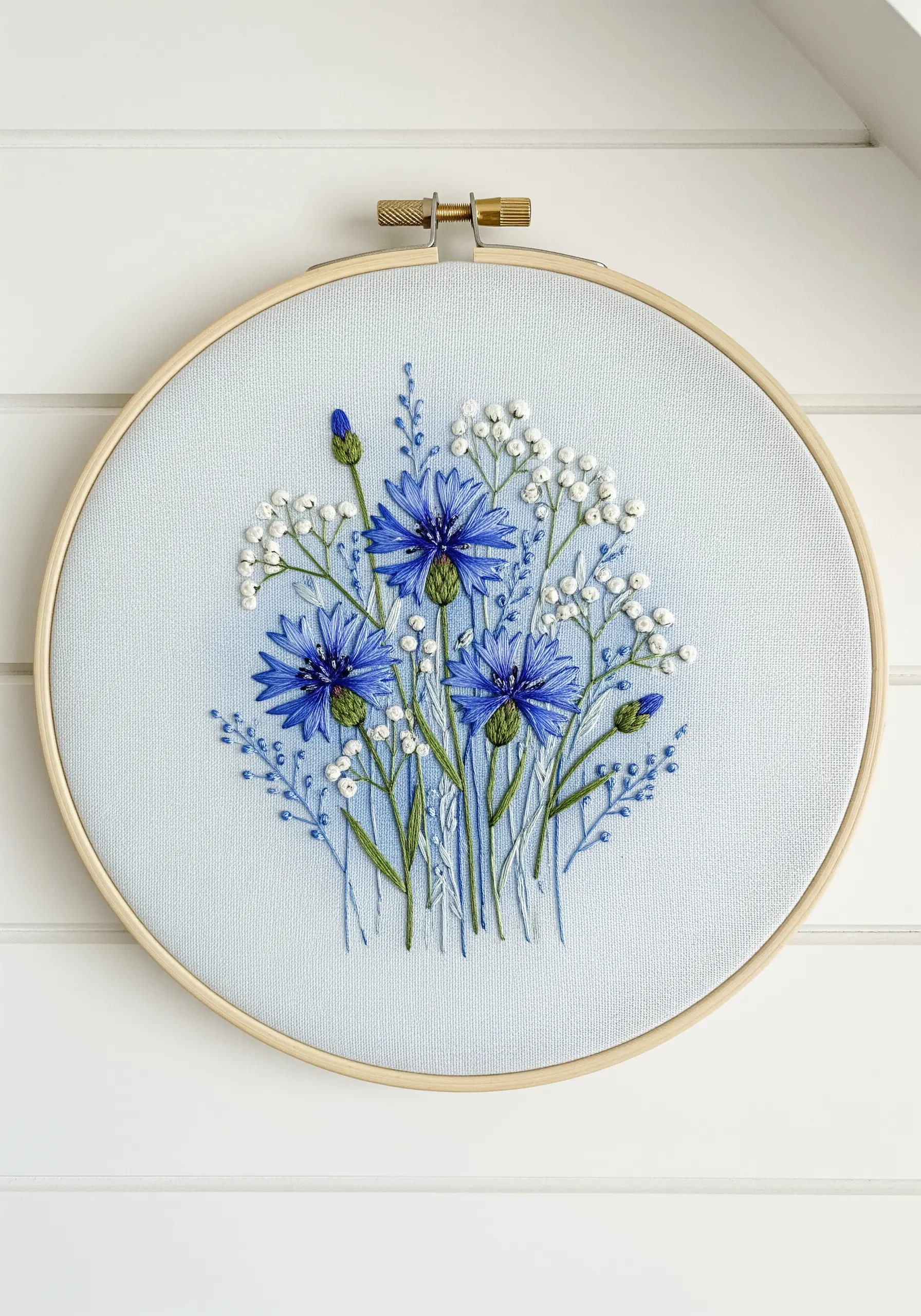 Delicate embroidery of blue cornflowers and white baby's breath on light blue fabric.