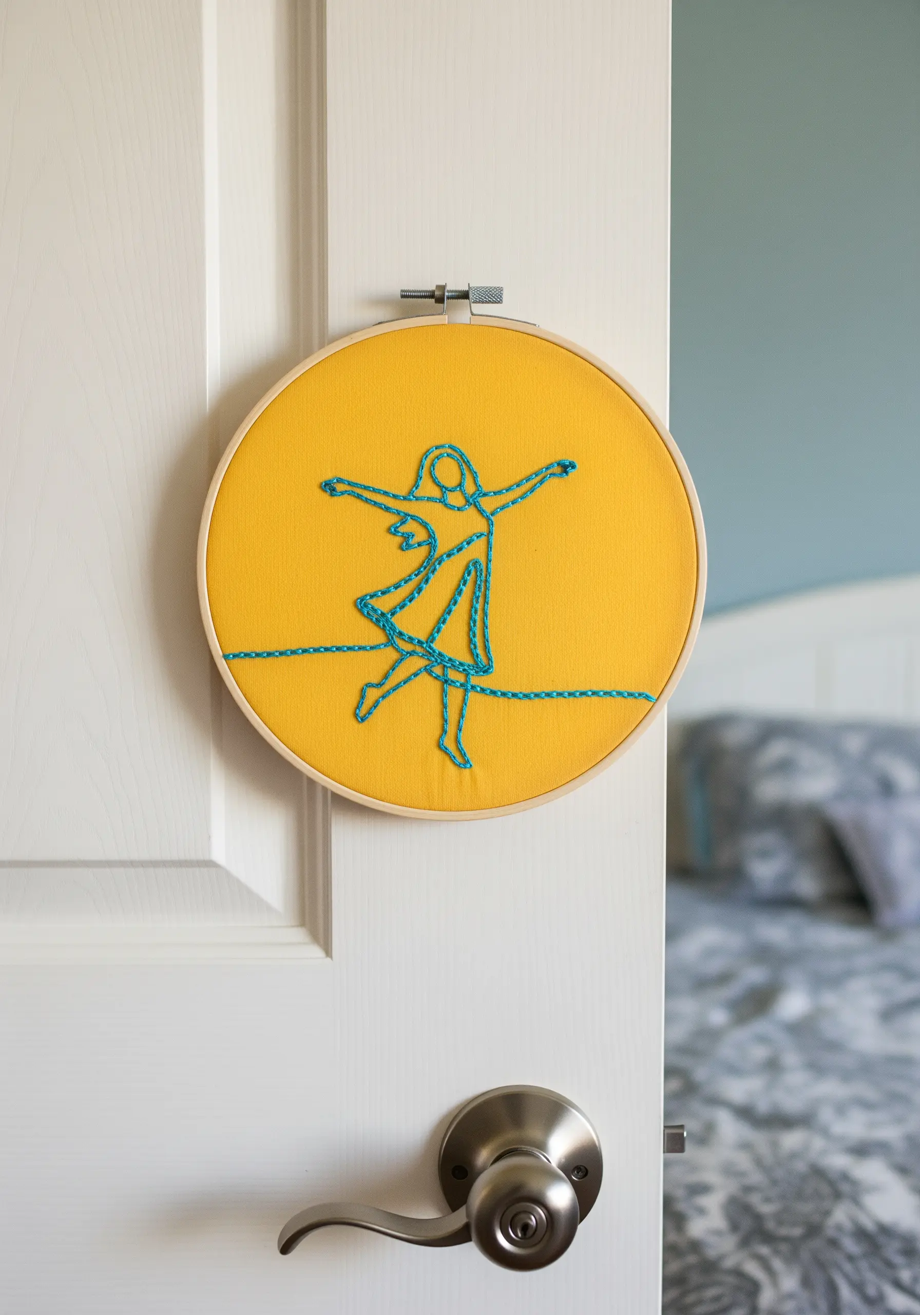 A continuous line art figure stitched in turquoise on a bright yellow fabric background.