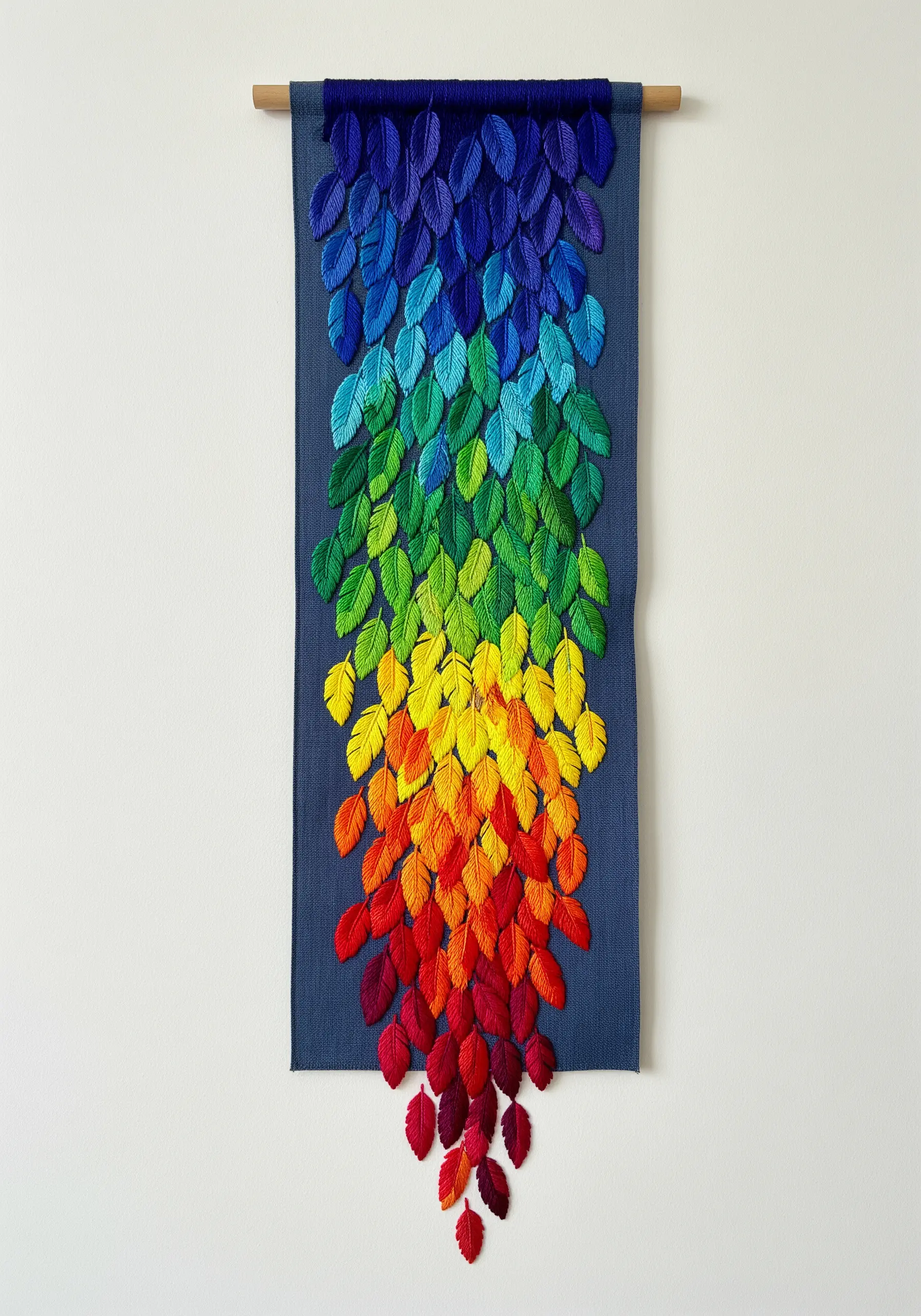 A wall hanging with embroidered leaves arranged in a cascading rainbow gradient.