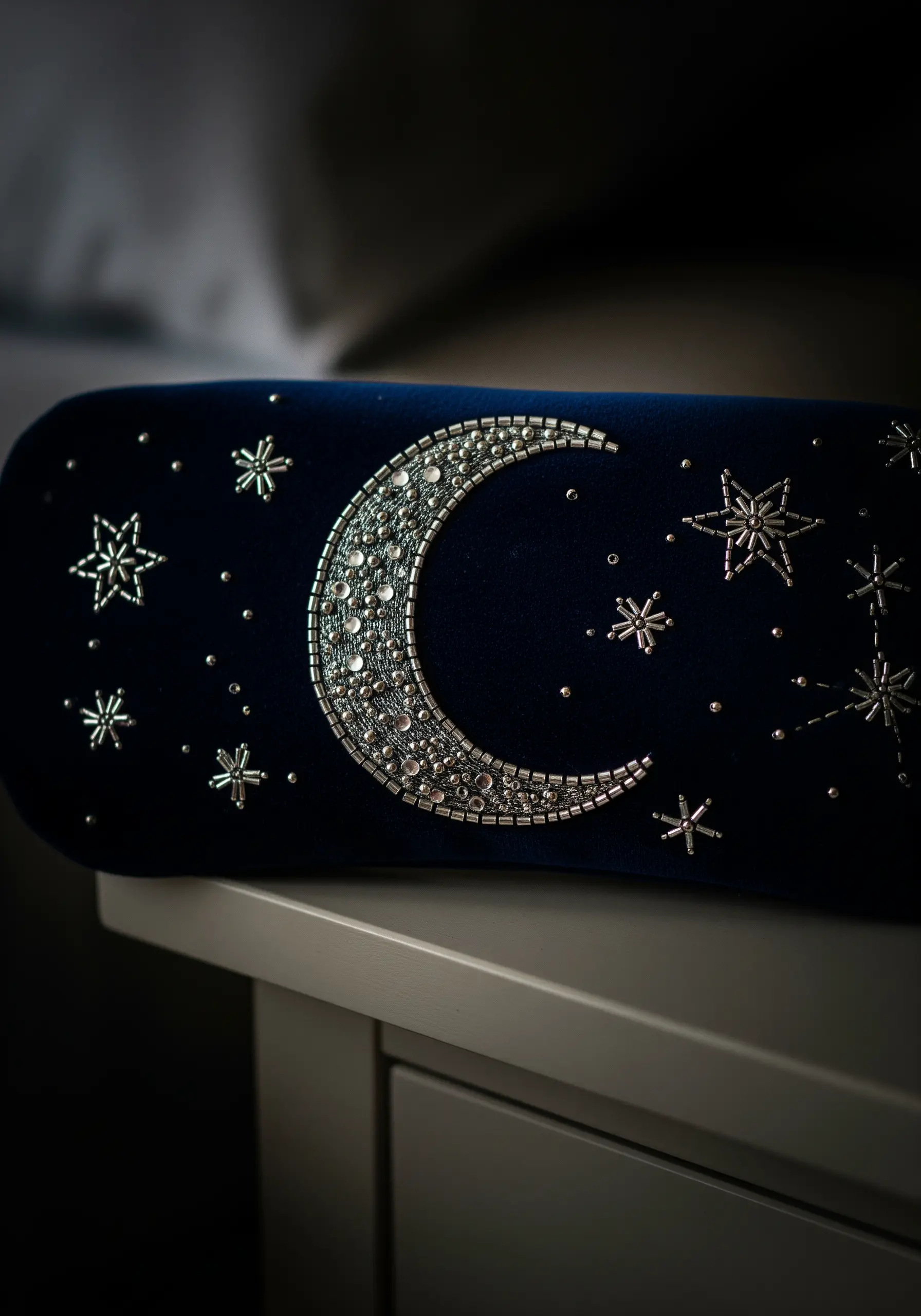 A navy velvet sleep mask embellished with a beaded silver crescent moon and starbursts.