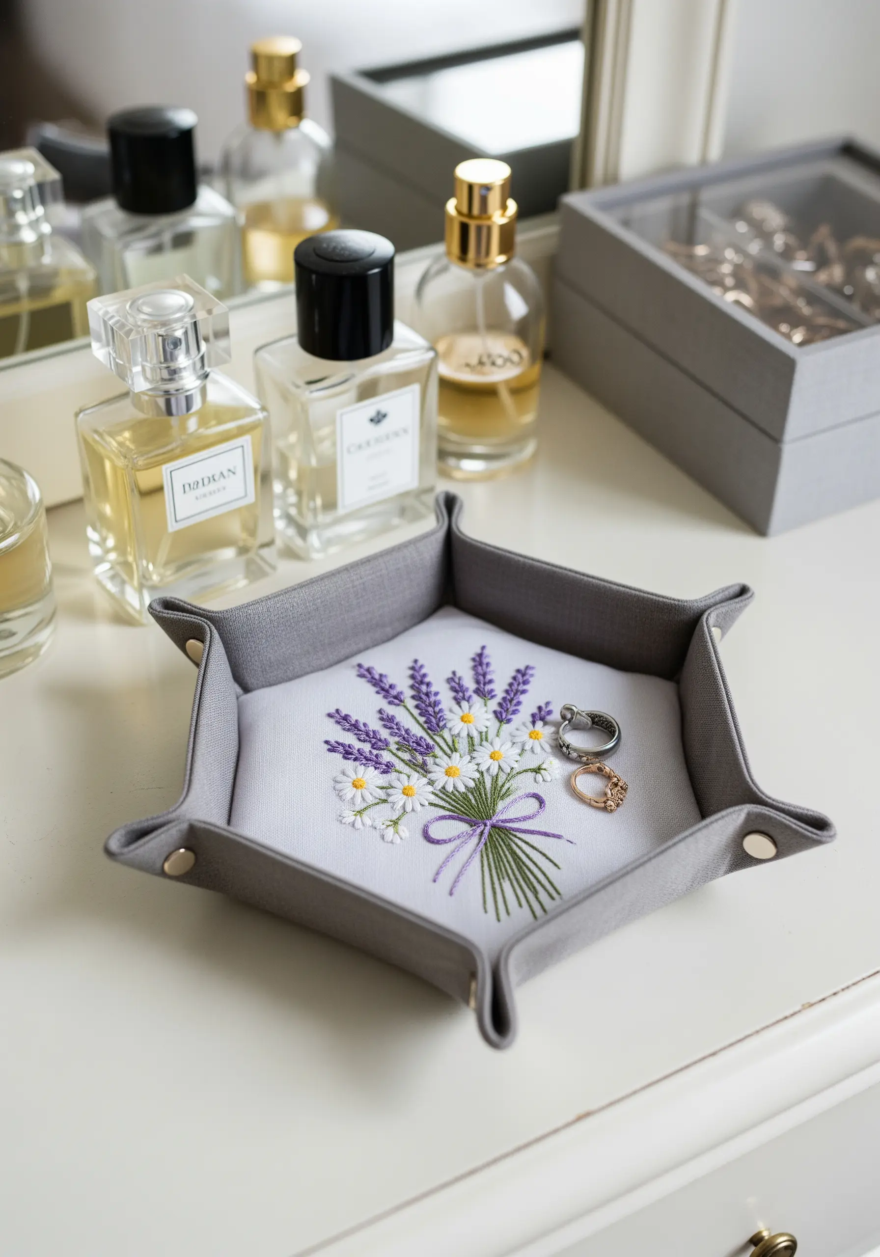 A gray fabric valet tray with a small embroidered bouquet of lavender and daisies in the center.